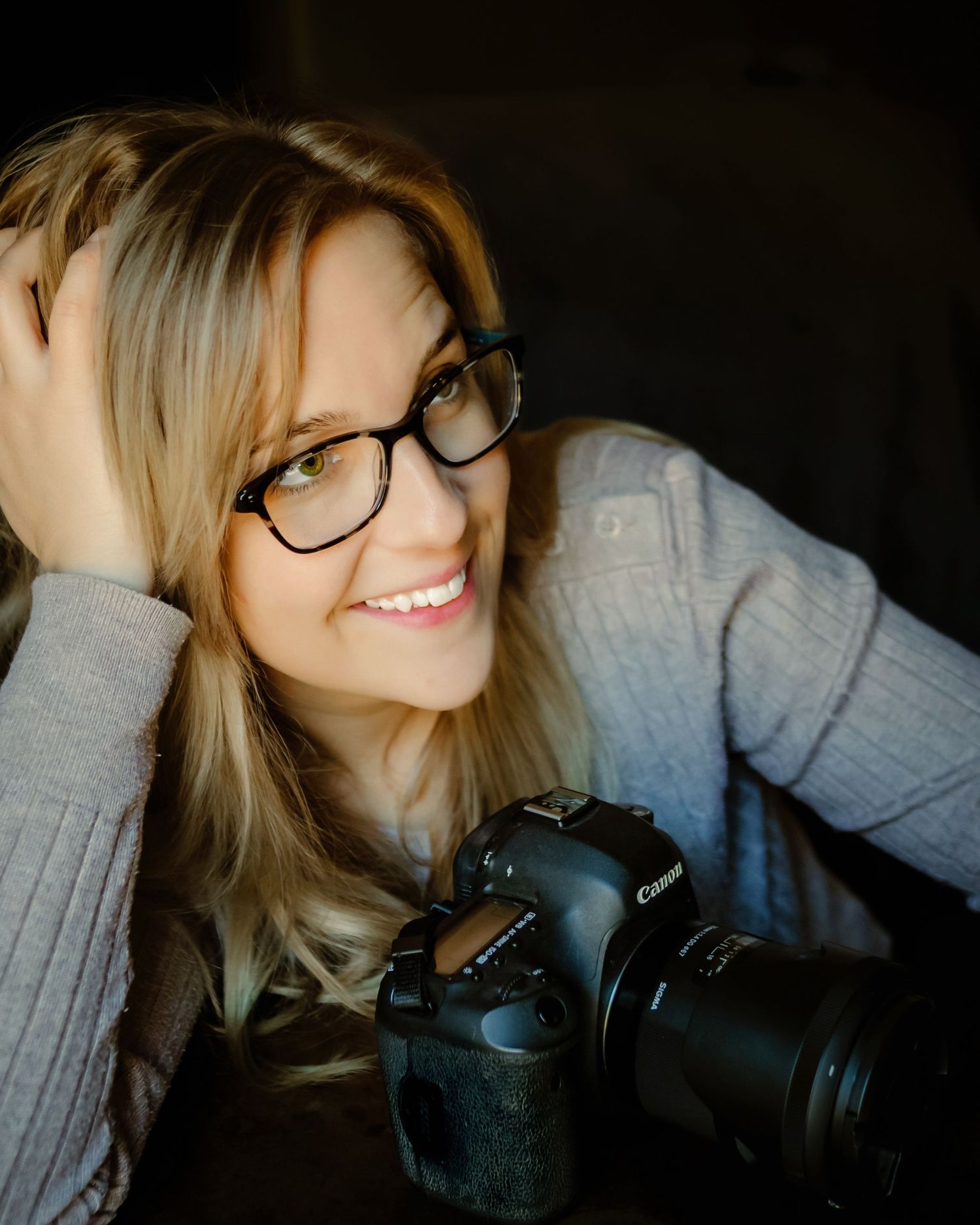 A Keller, Texas photographer in a gray sweater holds a professional DSLR camera while posing for self portraits in Fort Worth, Texas.
