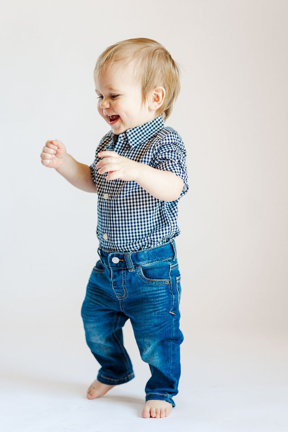 Energetic baby in blue outfit laughs while crawling on white background.