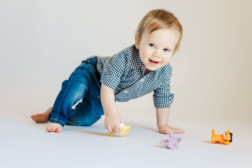 Baby plays with orange toy while crawling on white background.