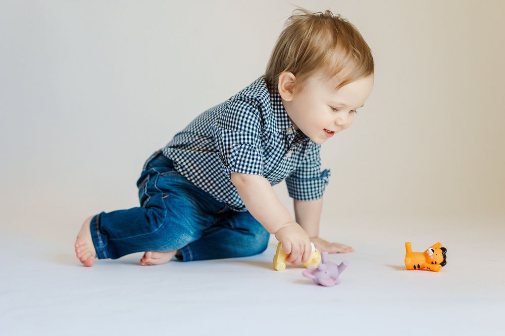 Baby reaches for small orange toy while crawling on white surface.