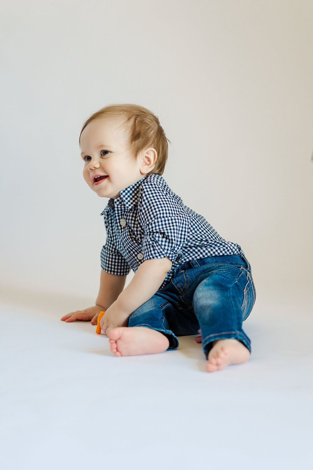 Happy baby in blue outfit explores white studio setting.