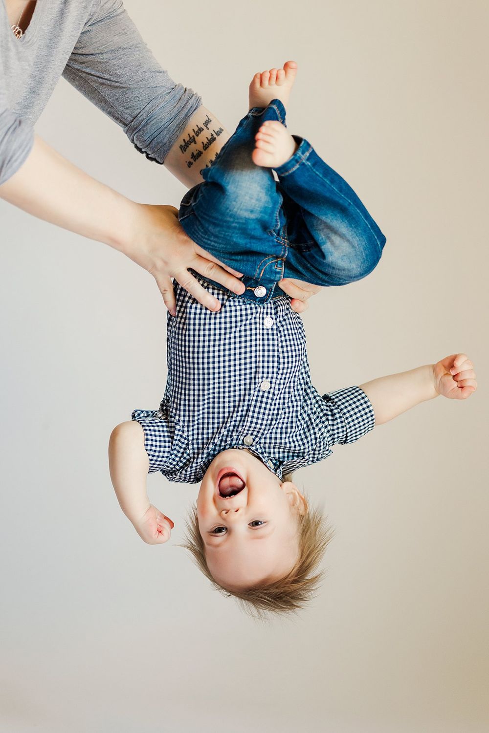 Playful upside-down moment with baby wearing gingham outfit.