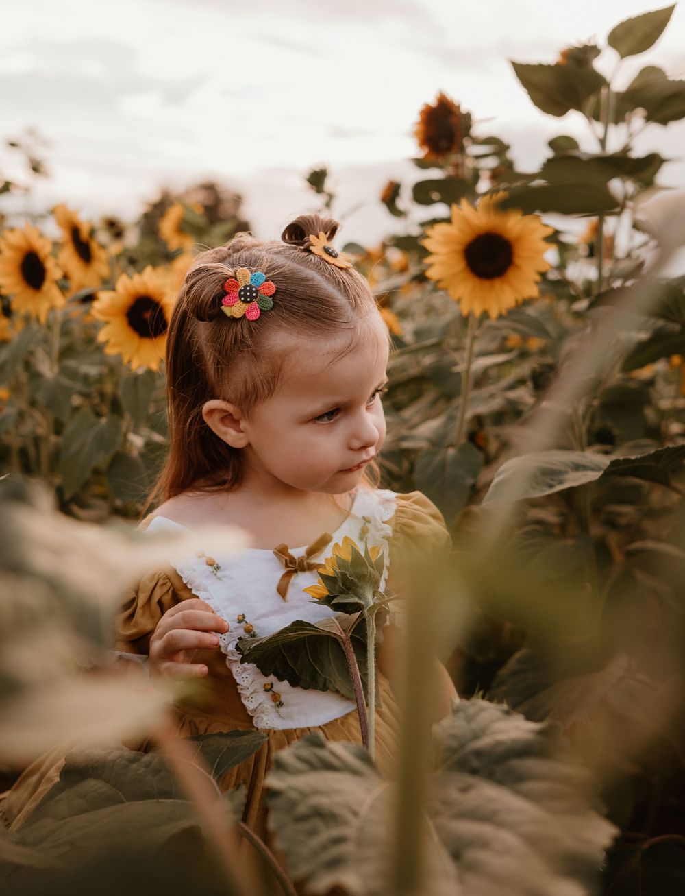 A child in a white dress explores a vibrant sunflower field during golden hour, creating a whimsical summer scene.