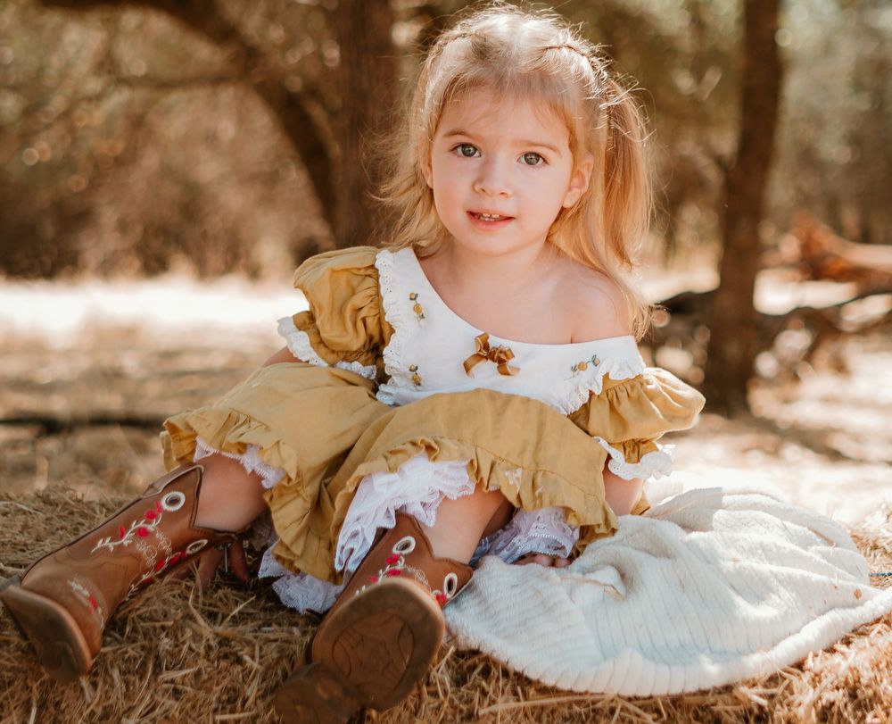Vintage-style photo series showing a child in a blue dress with ruffles sitting on autumn ground in warm sunlit setting.