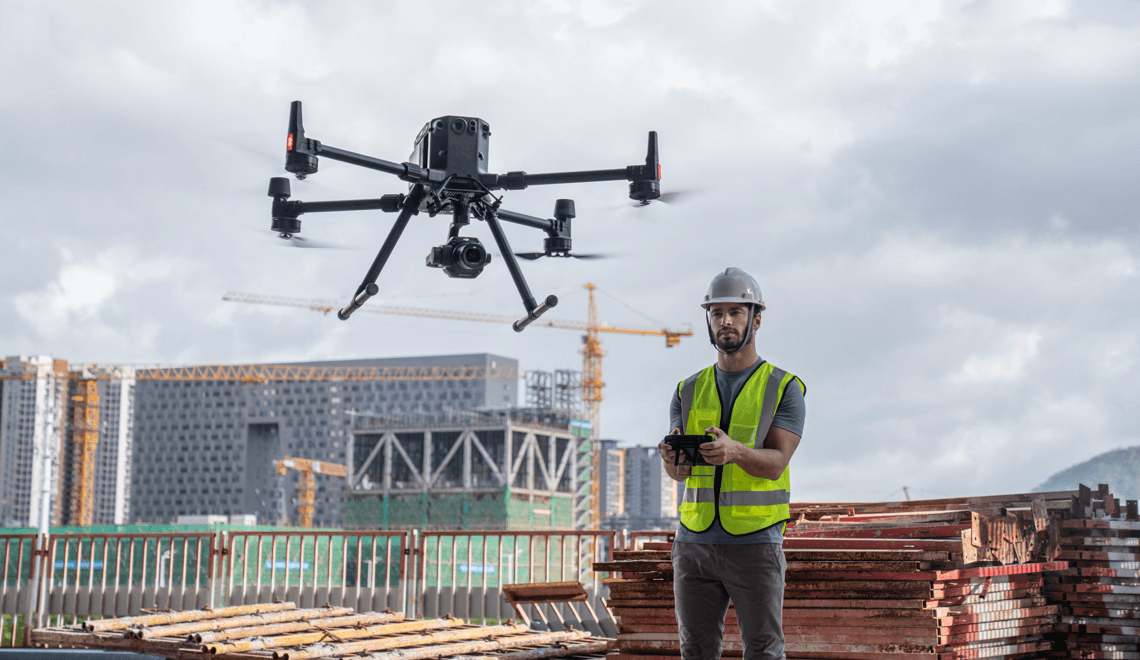 Commercial drone hovering near construction site with operator in safety gear.