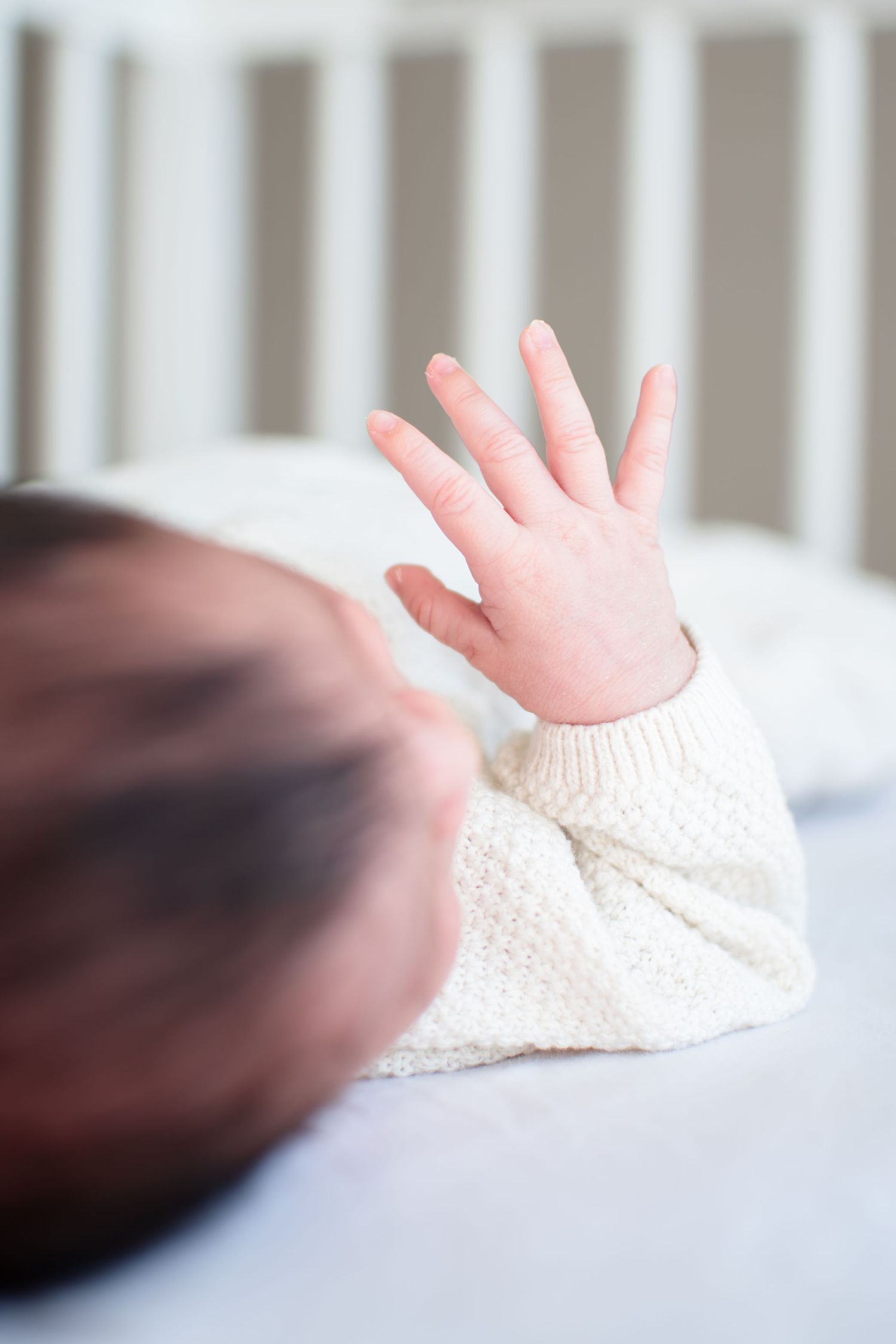 Baby stretches her fingers out while she sleeps contently in her crib.