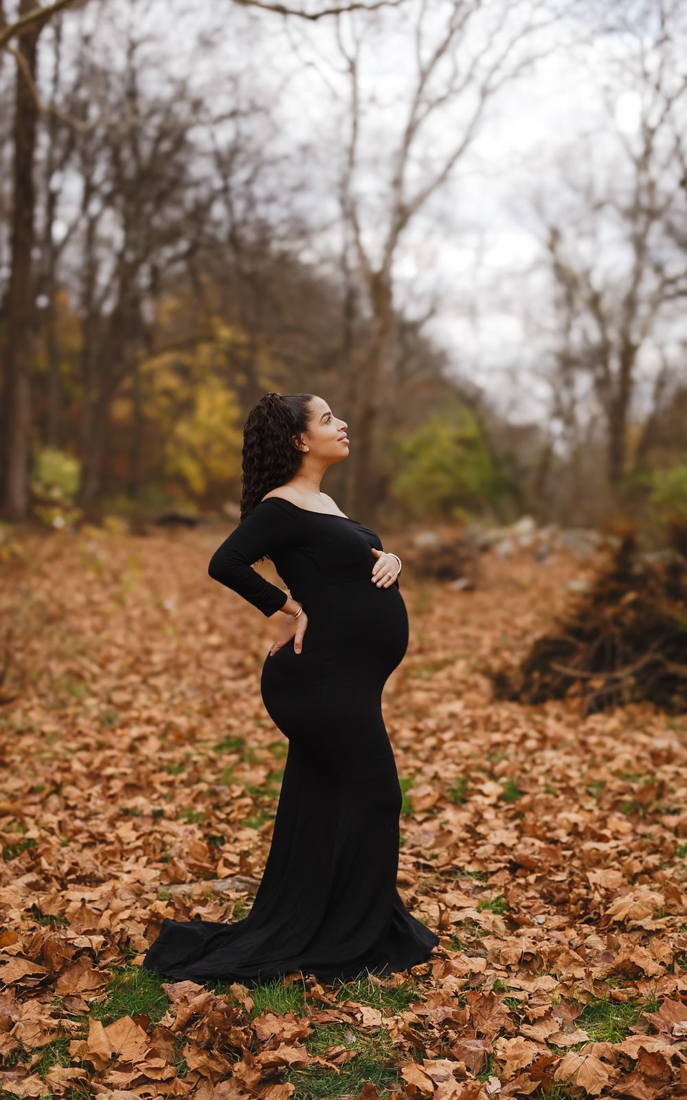 Maternity portrait in a black gown among fall leaves in Lemoyne