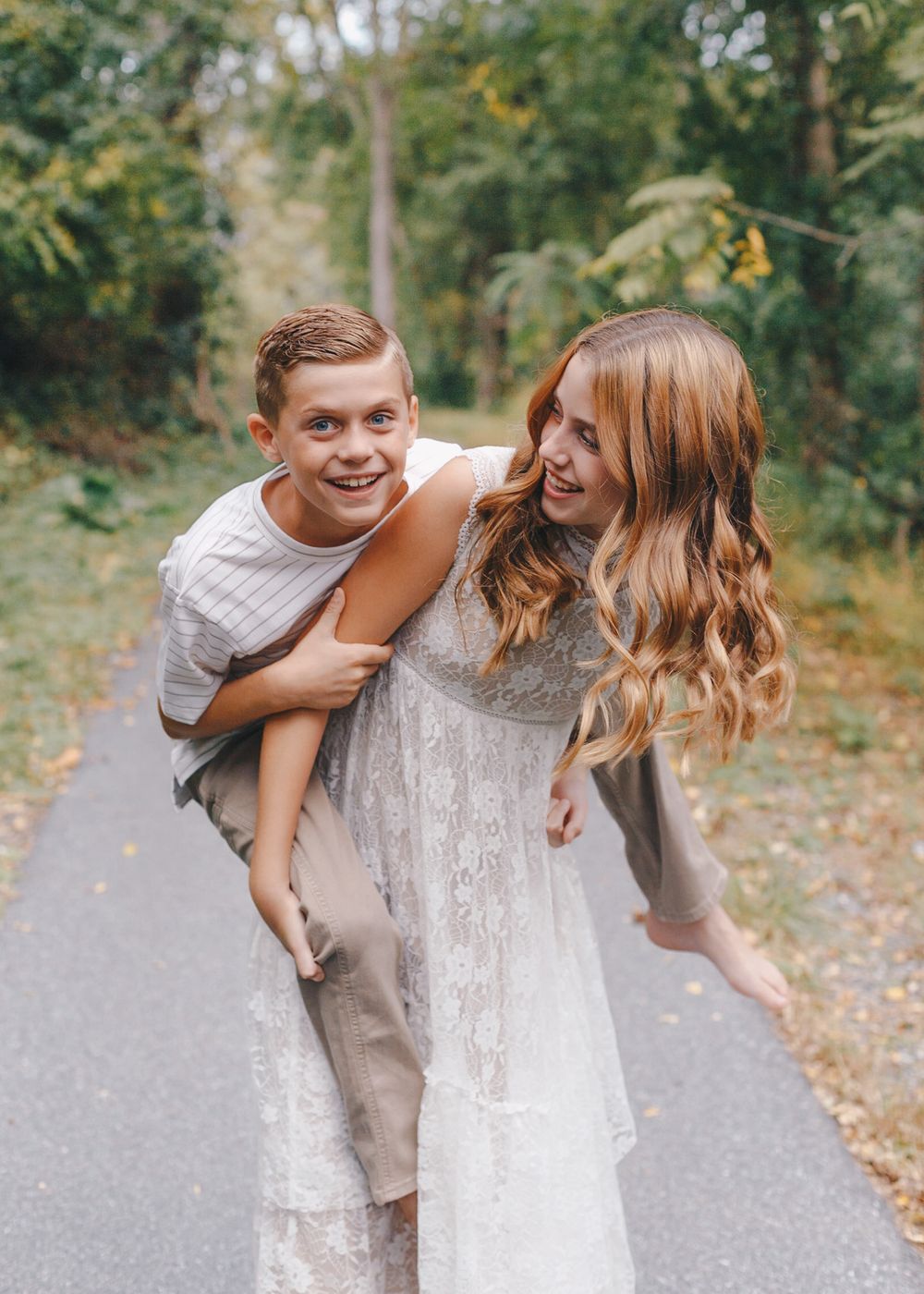 Siblings laughing during a piggyback ride on a Carlisle path