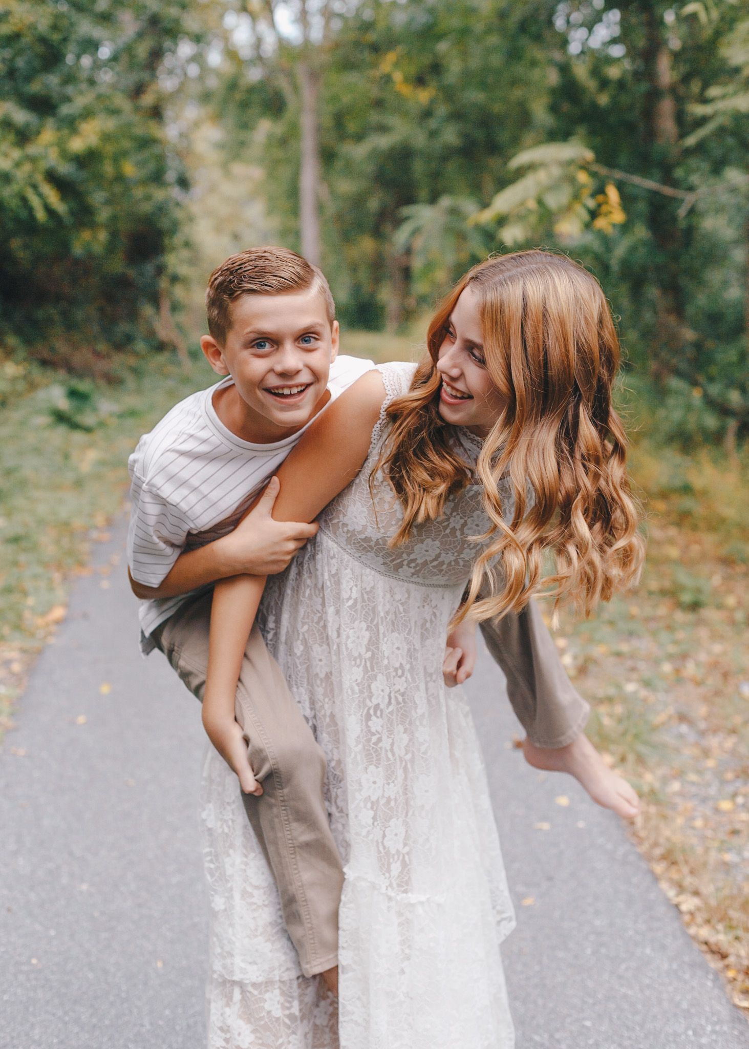 Siblings laughing during a piggyback ride on a Carlisle path