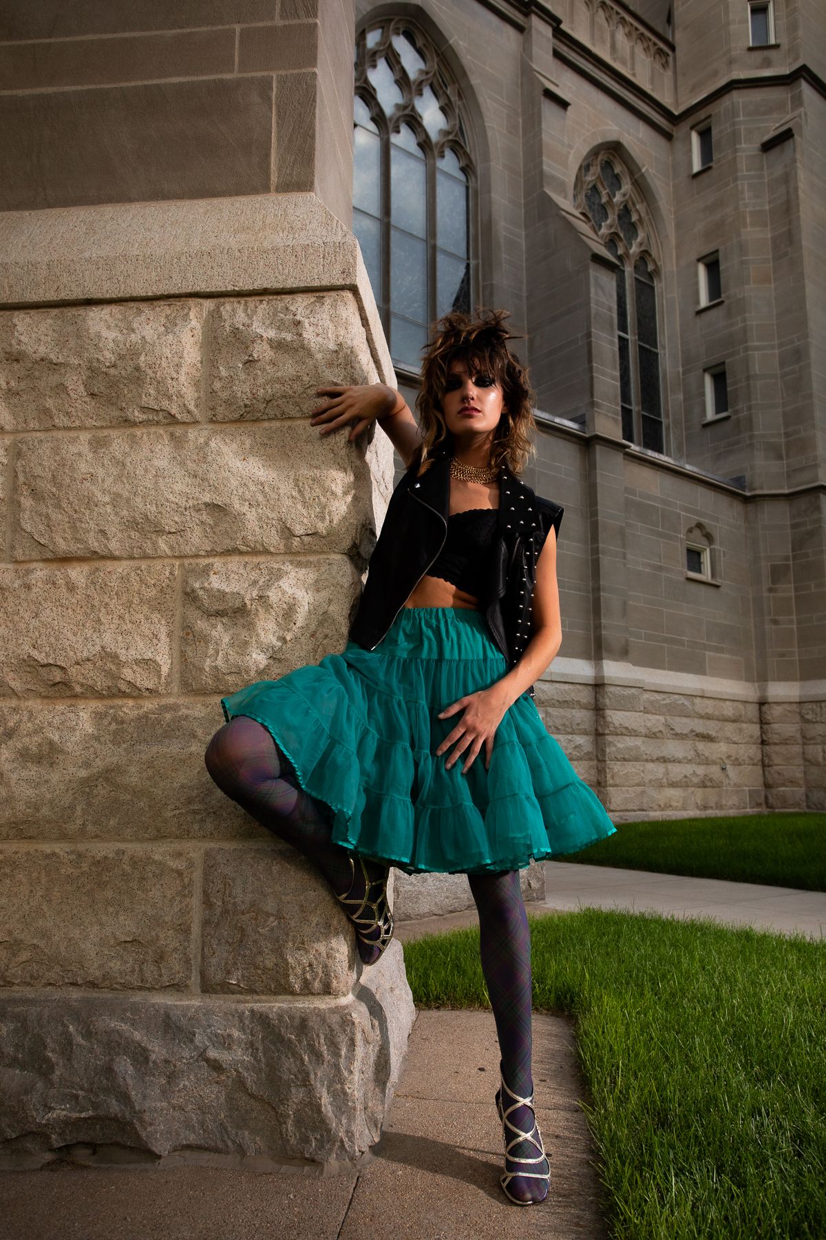 Fashion model in teal tutu skirt poses dramatically against gothic stone architecture.