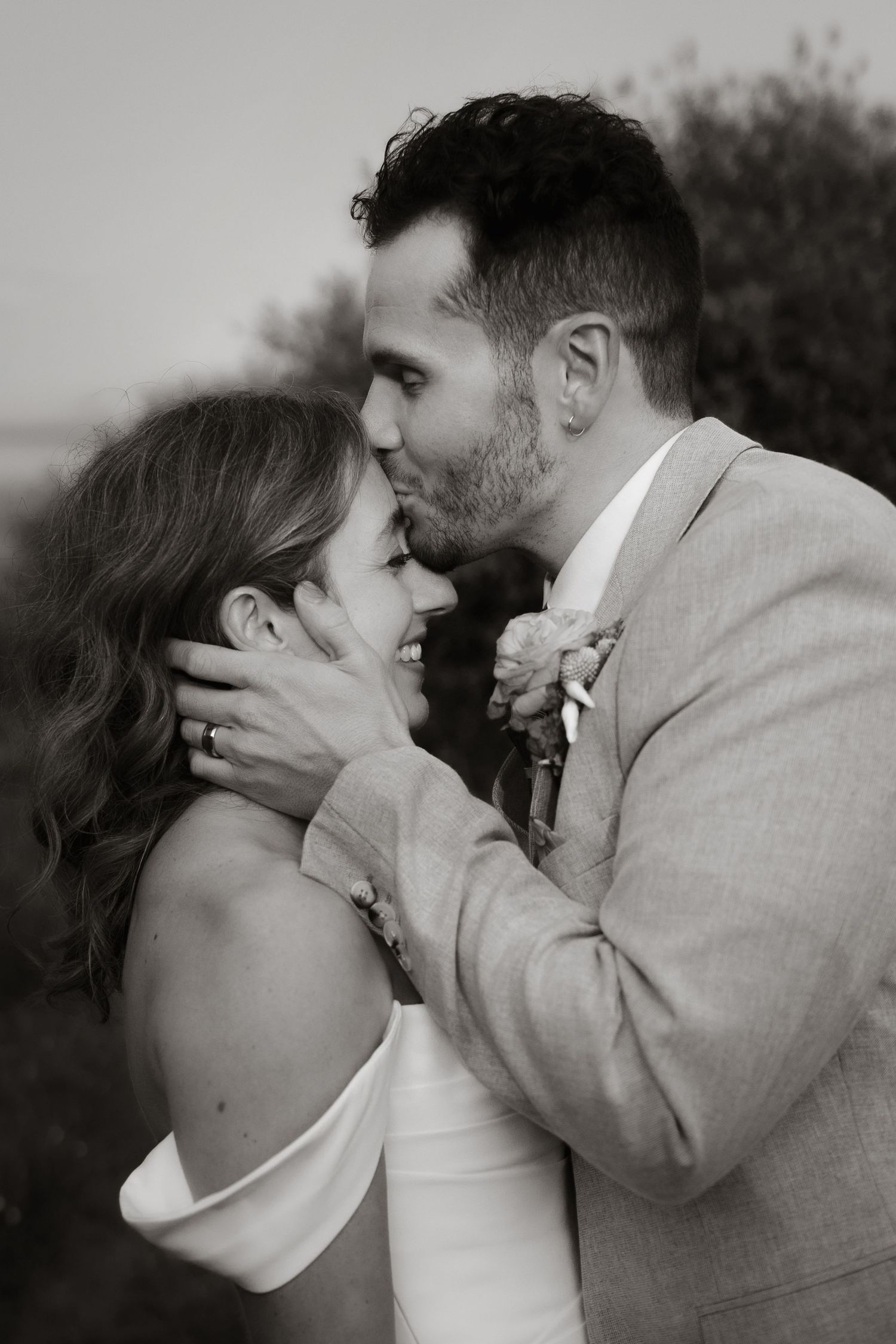 A couple embraces in front of a garden gazebo, with the person in a floral dress holding an autumn-themed bouquet.