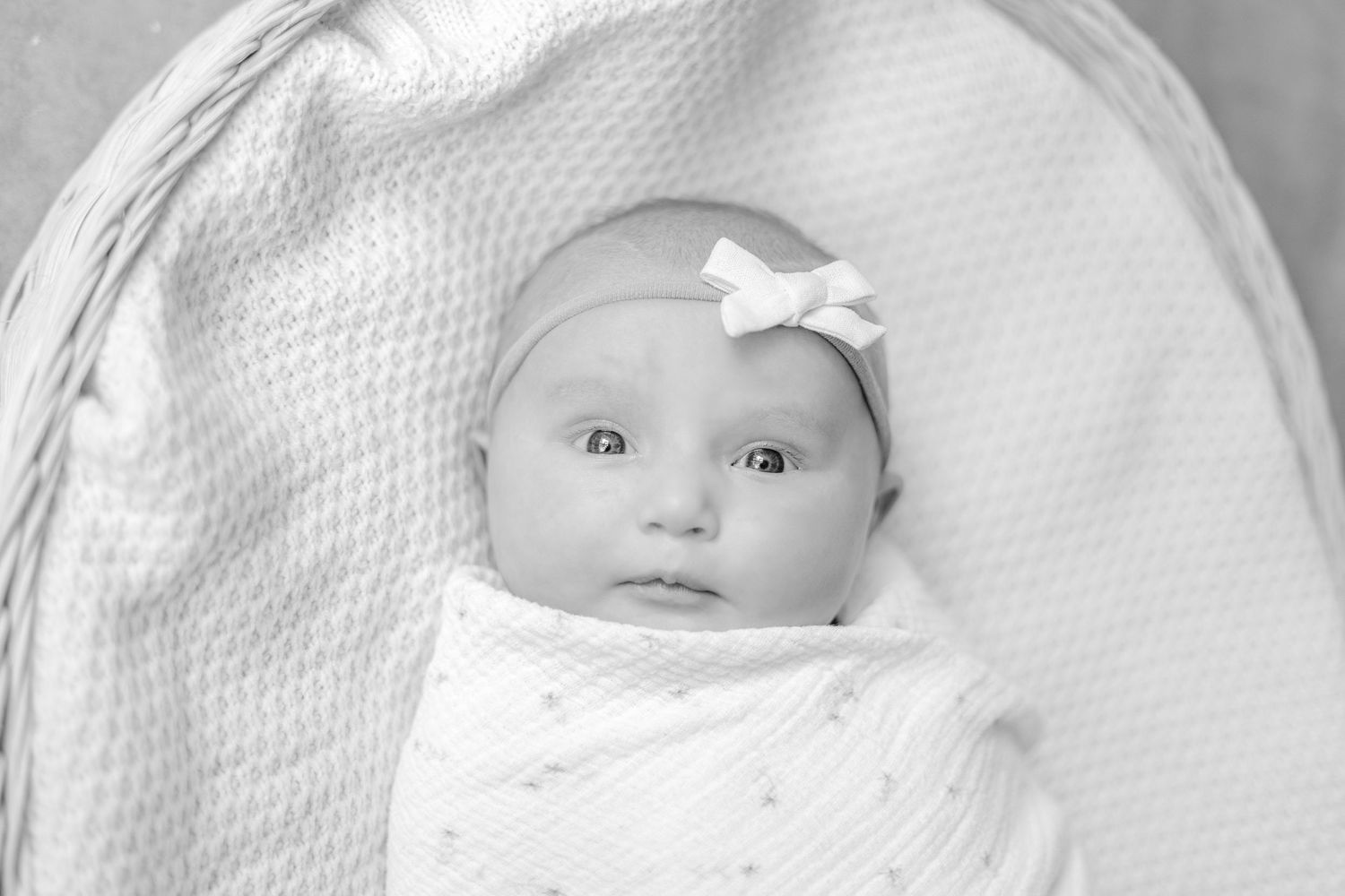 Baby lying on textured white blanket during minimalist black and white photo session.