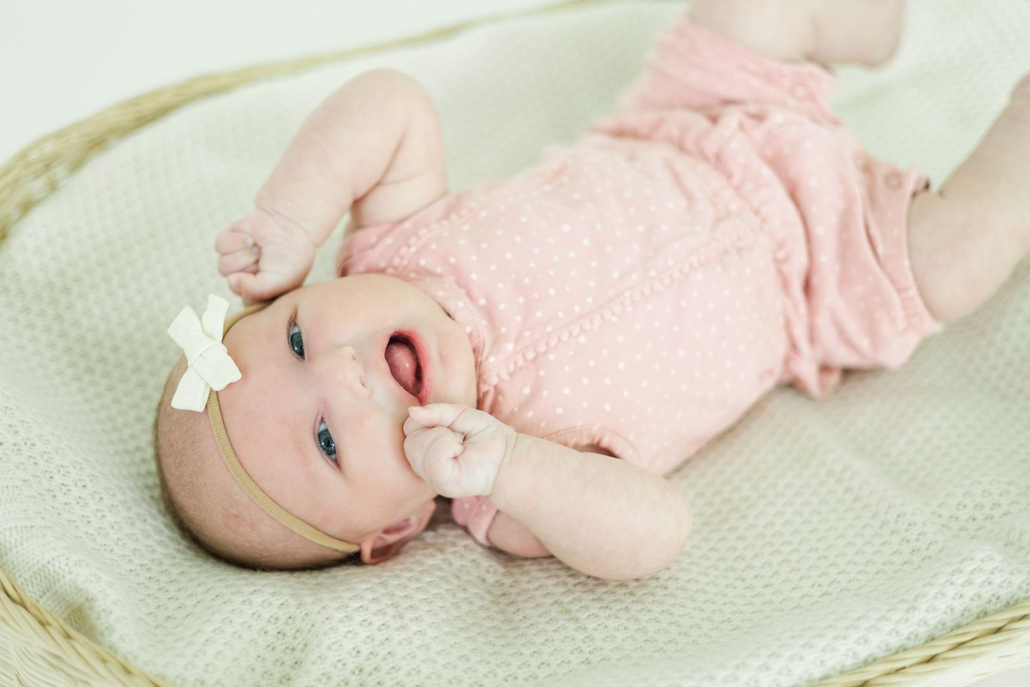 Baby in pink outfit resting in white wicker basket on mint green blanket.