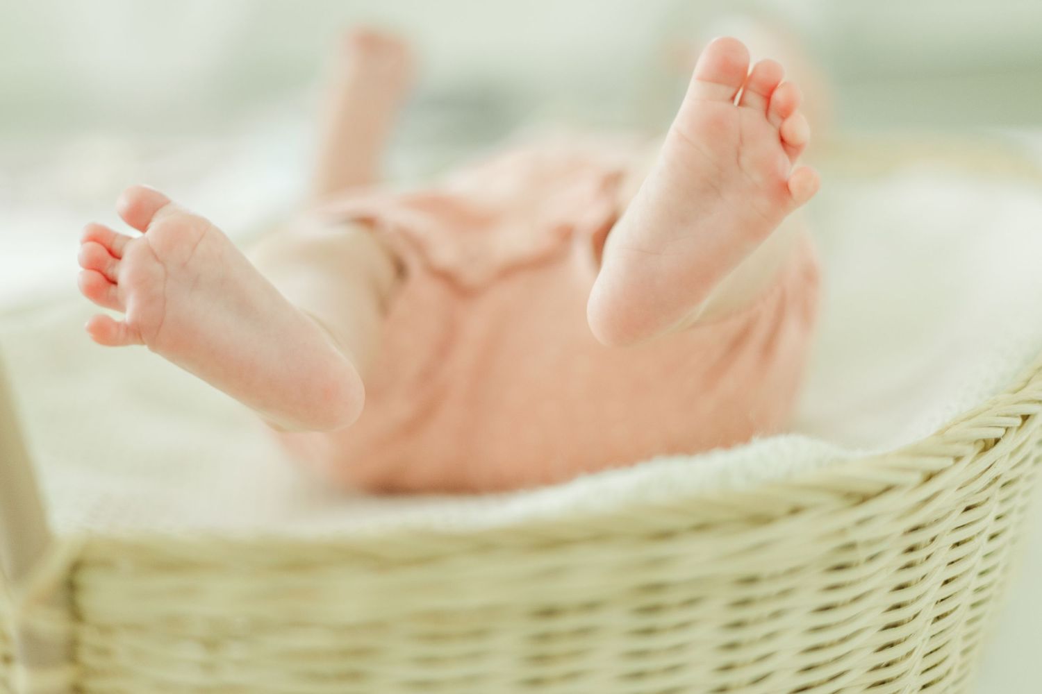 Close-up of baby's feet and legs in white wicker basket during newborn photoshoot.
