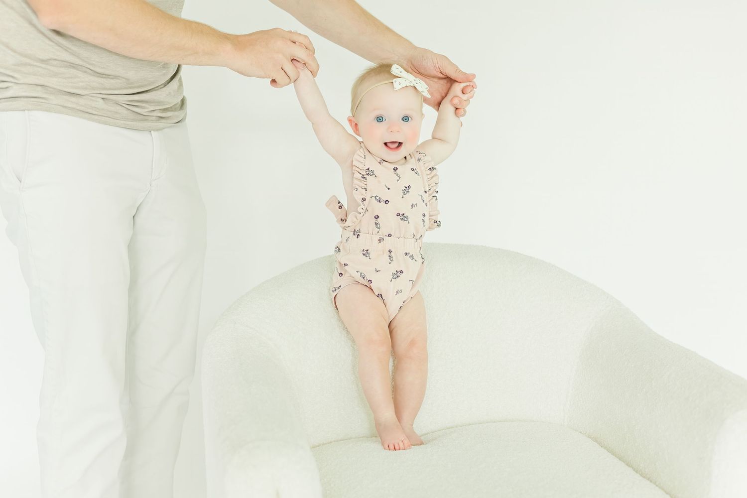 Baby in floral outfit being lifted in the air against white background.