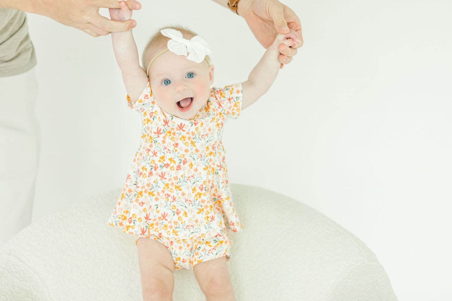 Baby wearing floral outfit playing happily on white furniture.