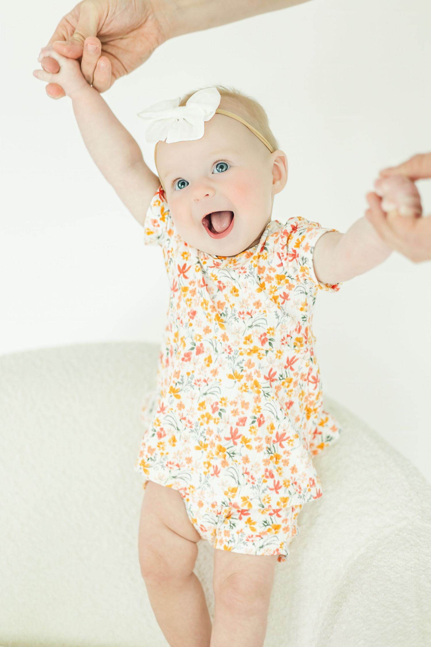 Baby wearing floral romper lies on white blanket showing joyful expressions.