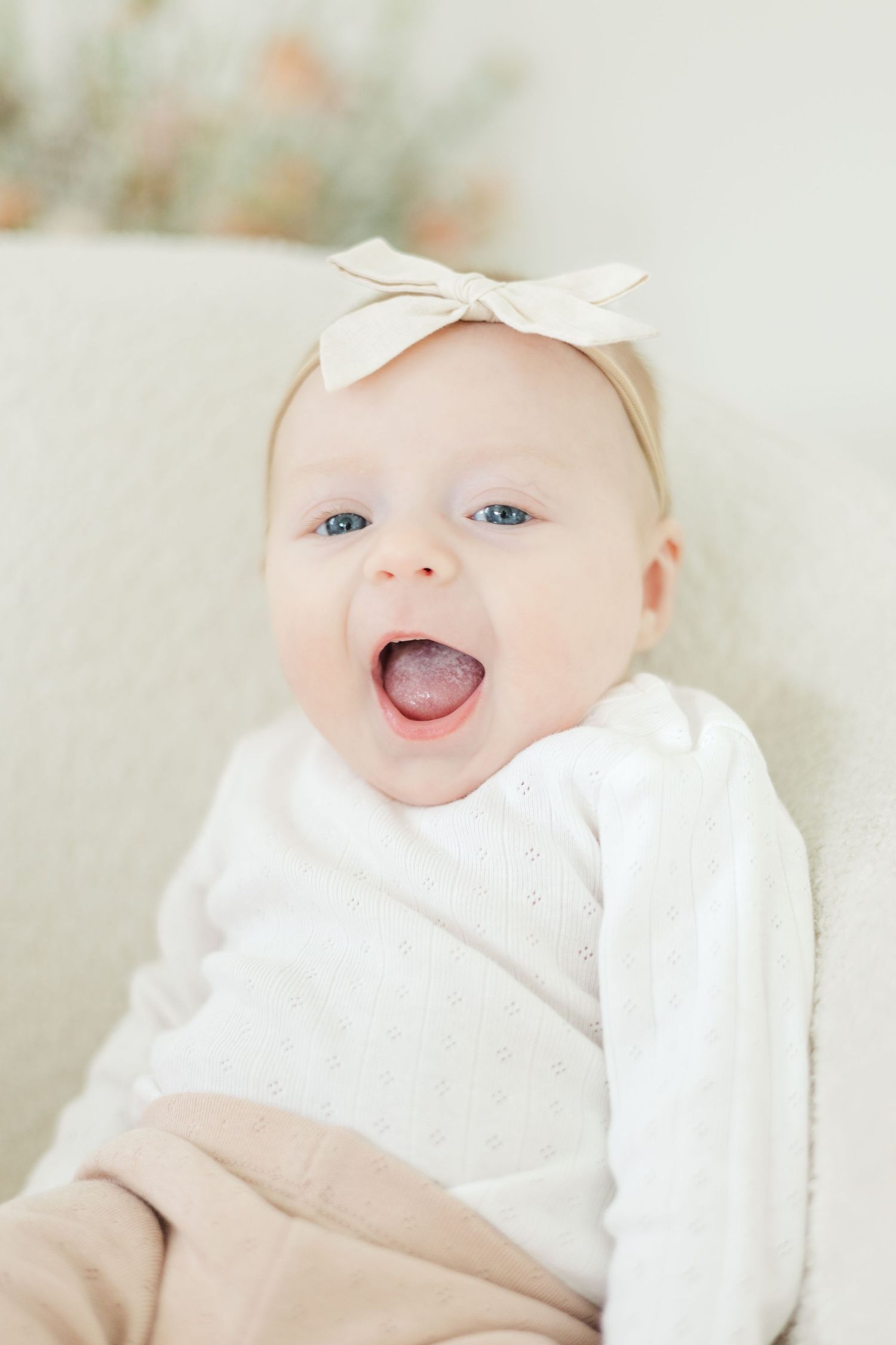 Sweet baby in white outfit and bow smiling and showing personality in bright studio portraits.