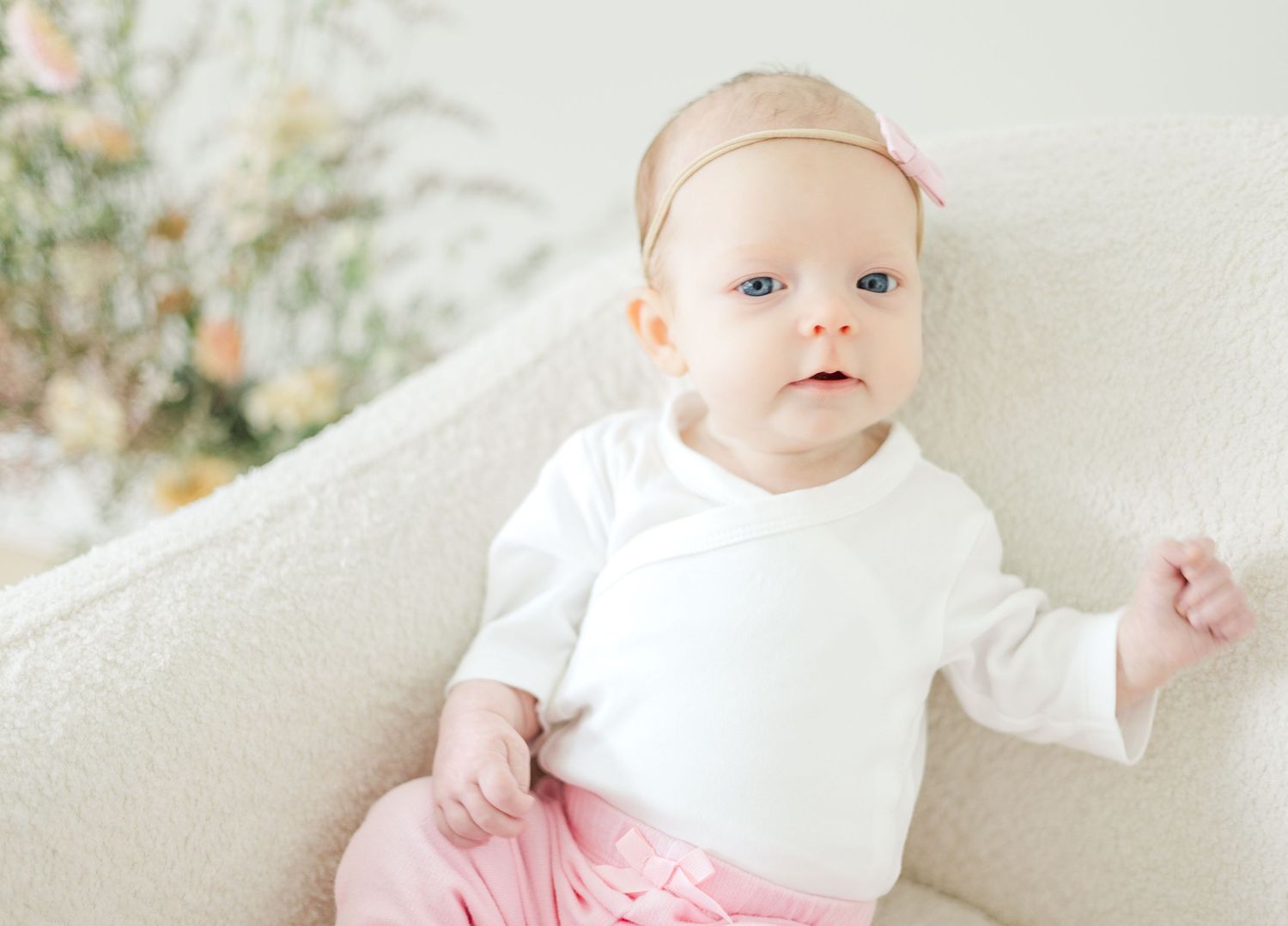 Baby in white outfit and pink accents photographed against bright minimal studio backdrop.