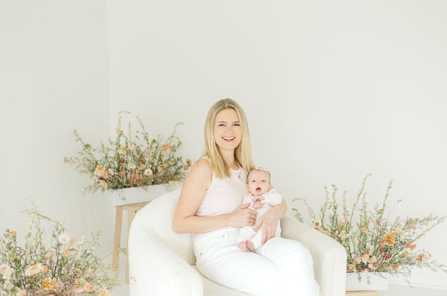 A series of tender mother and baby portraits in a bright white studio with delicate floral accents.