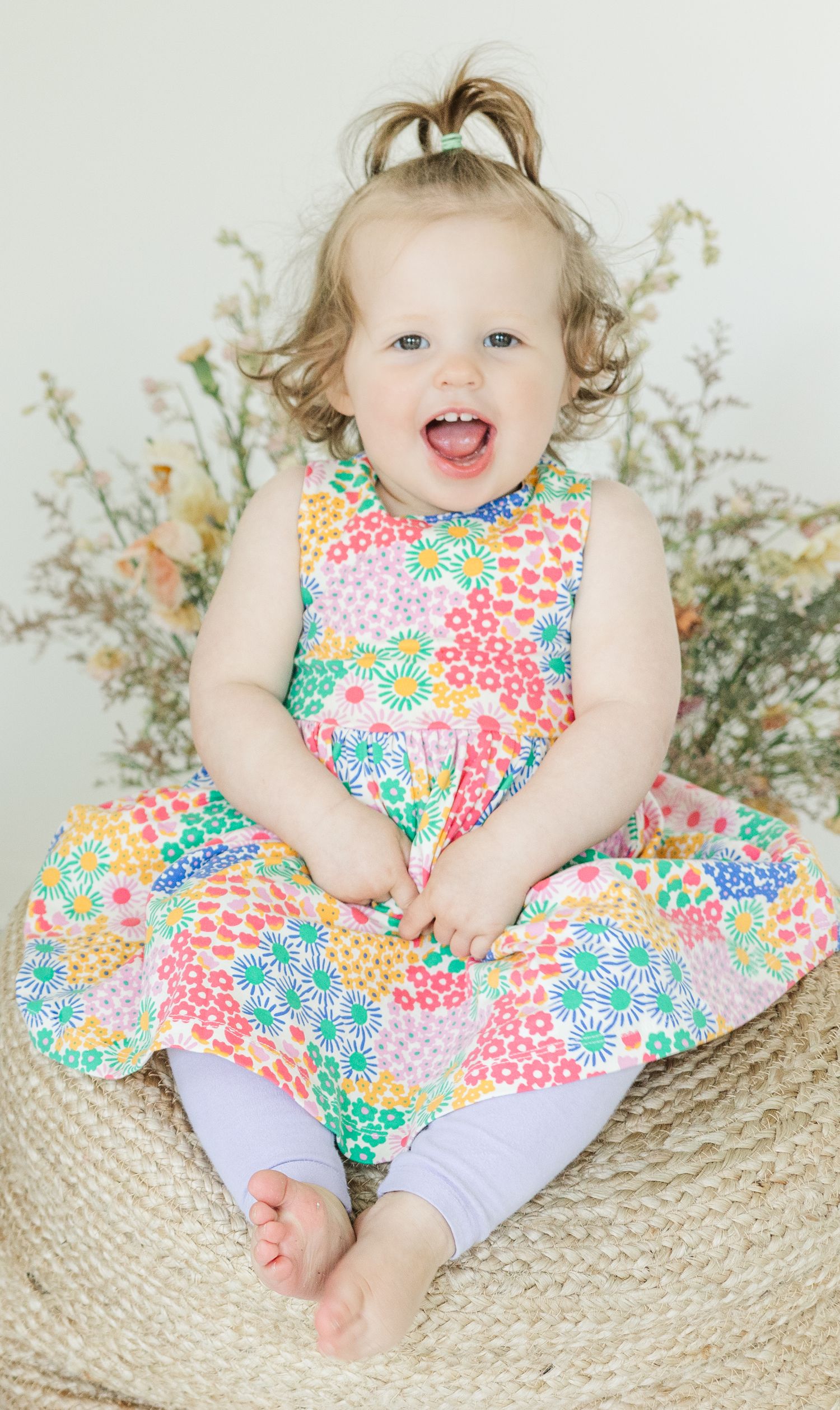Happy expressions while wearing a colorful floral dress on a woven basket seat.