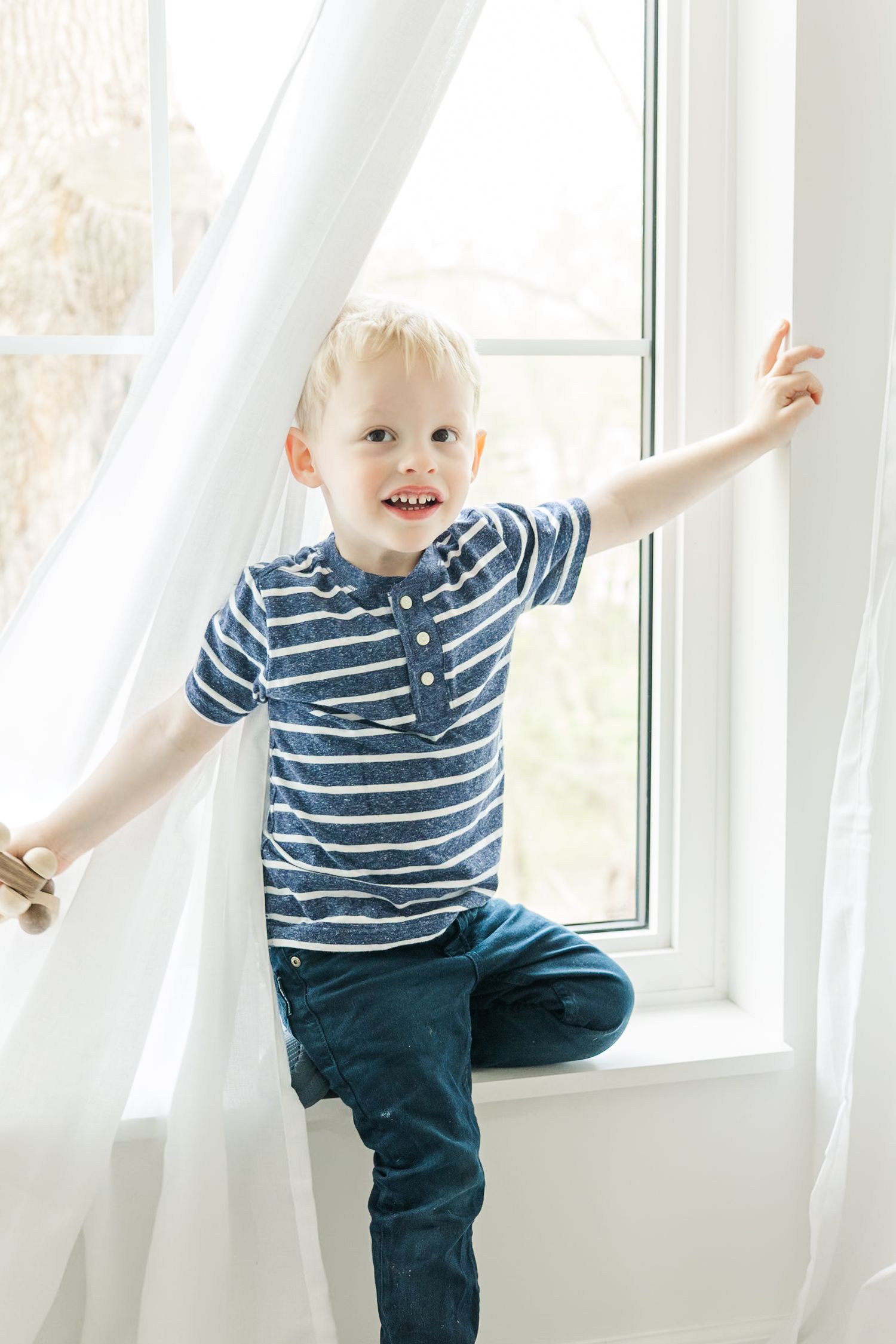 Playful poses in a blue striped shirt and jeans by a bright window.