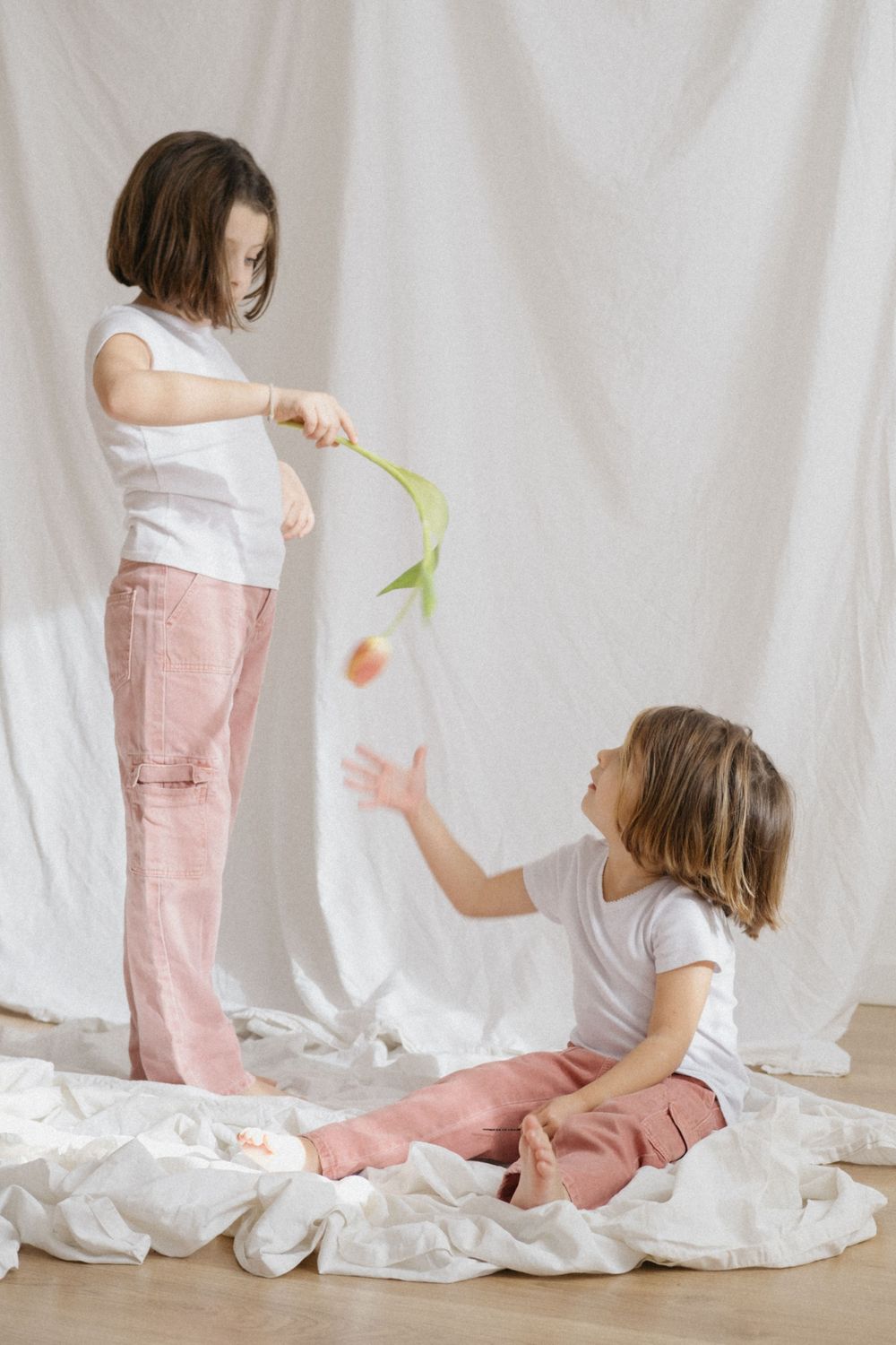 Hermanas vestidas a juego jugando con flores entre las sábanas tendidas