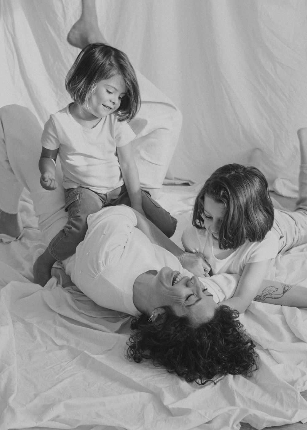Retrato en blanco y negro de una familia compartiendo un momento divertido sobre sábanas blancas.