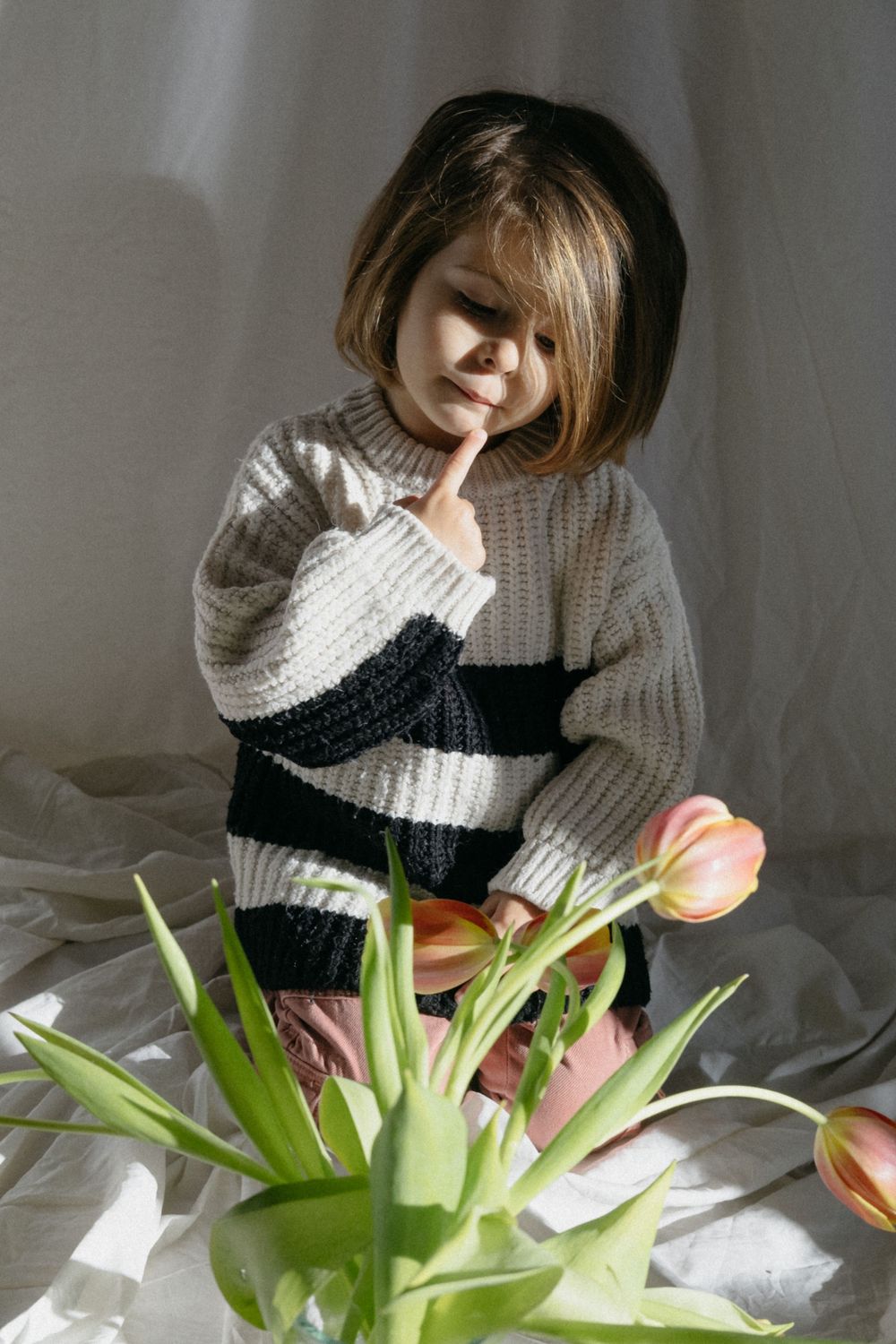 Niña con suéter de rayas admirando tulipanes rosados ​​bajo la luz natural