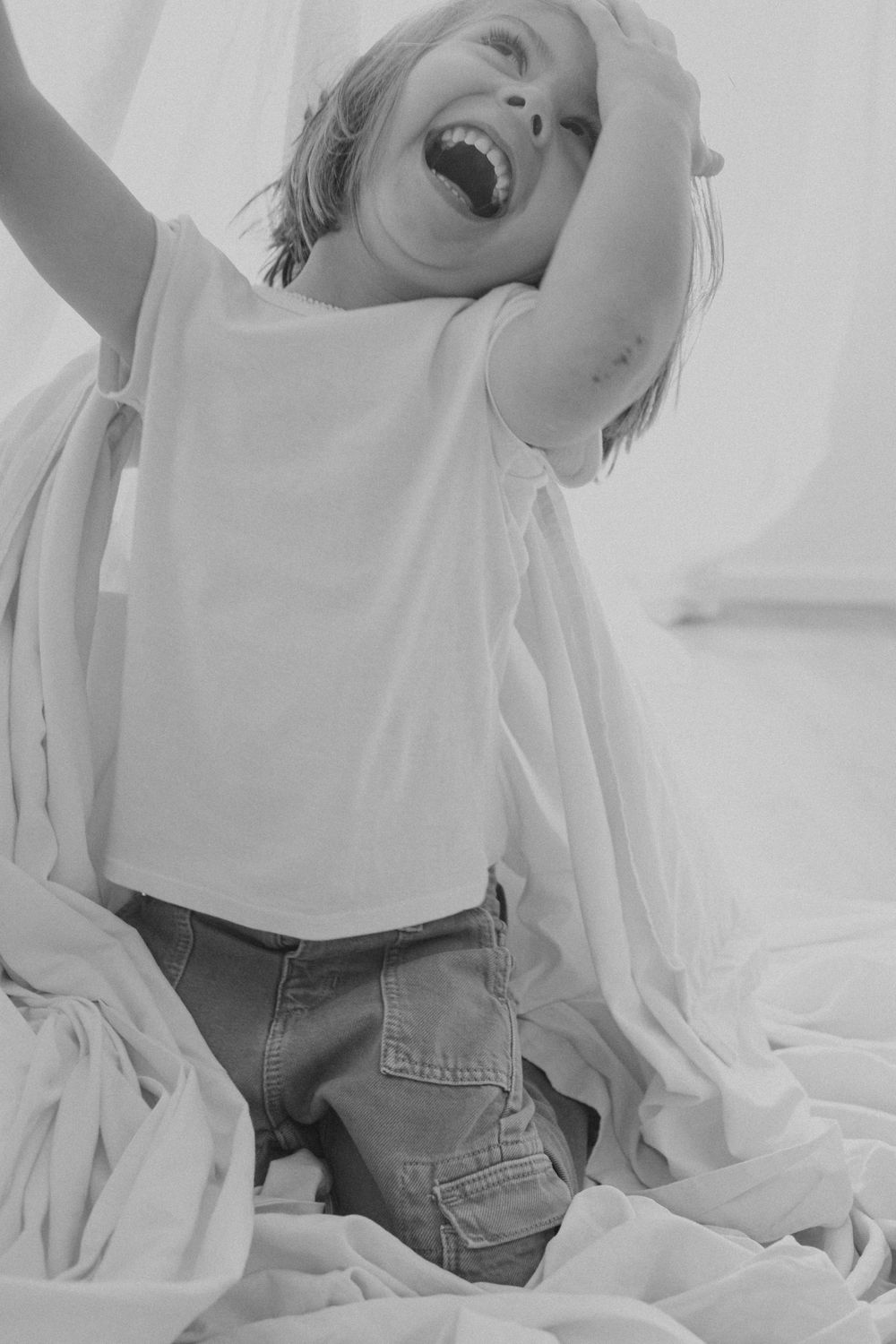 Fotografía espontánea en blanco y negro que captura una risa alegre entre una tela blanca.