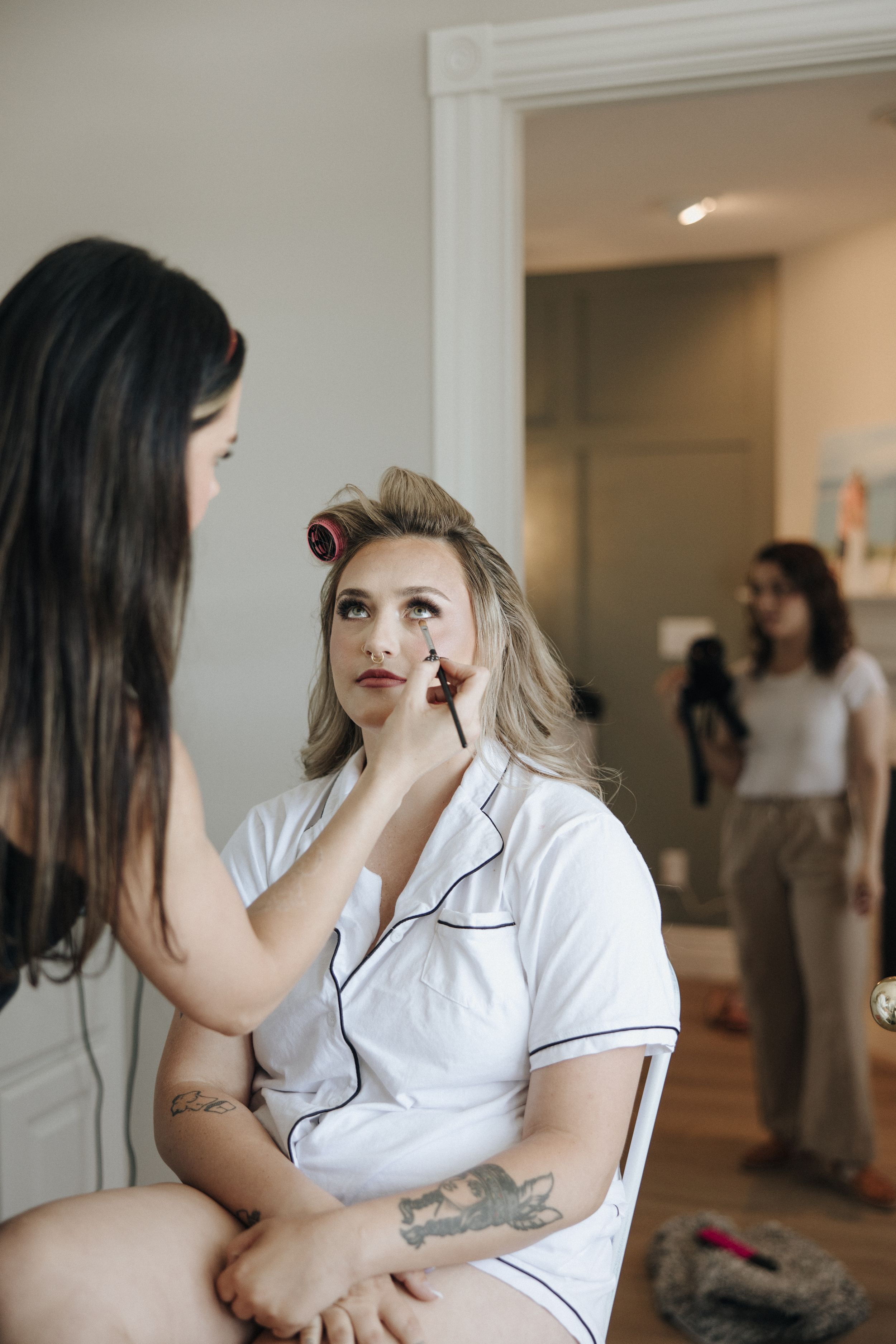 A makeup artist applies lipstick during wedding day preparations in a bright room.