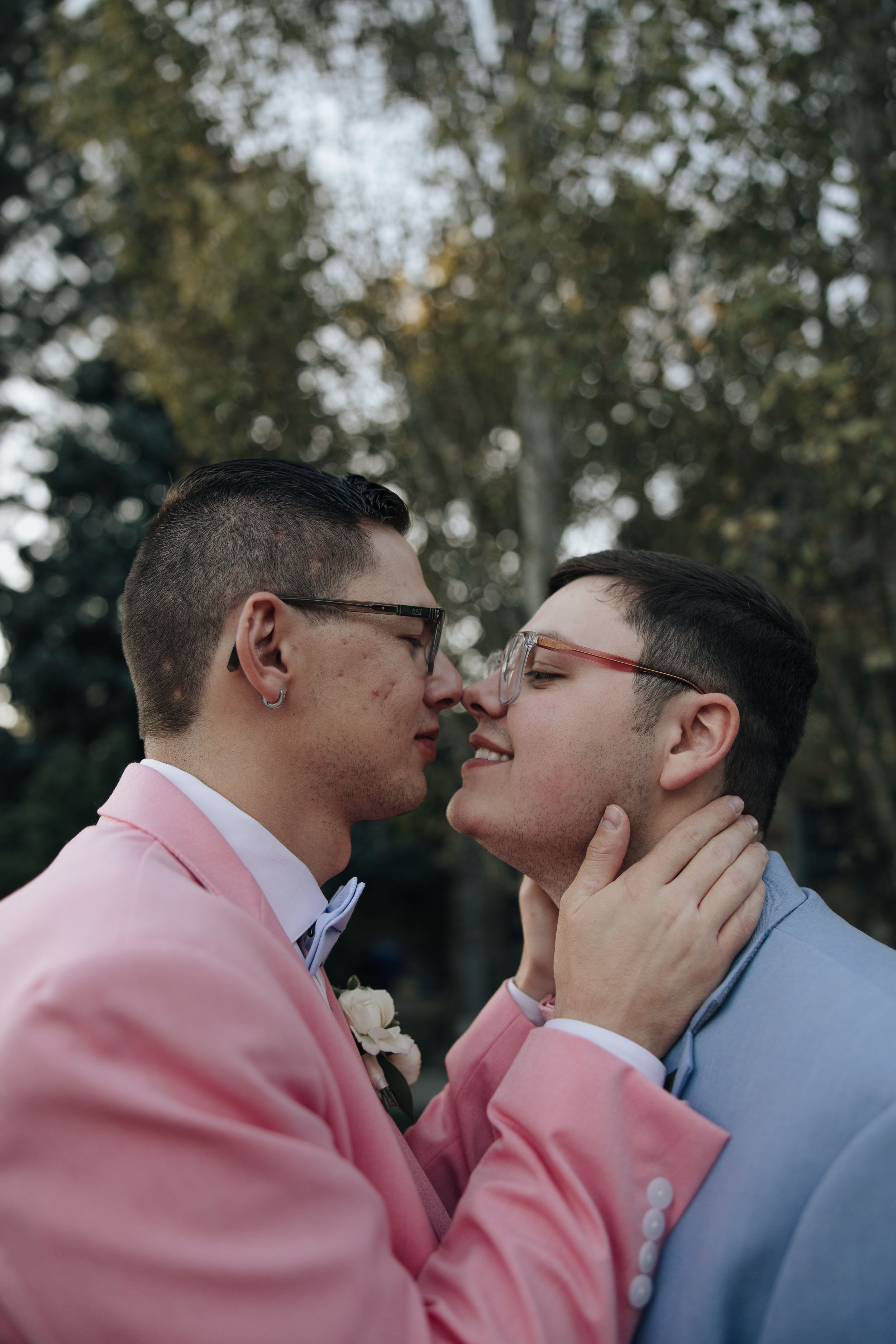 A tender moment between two people wearing matching pink blazers amid a blurred natural backdrop.