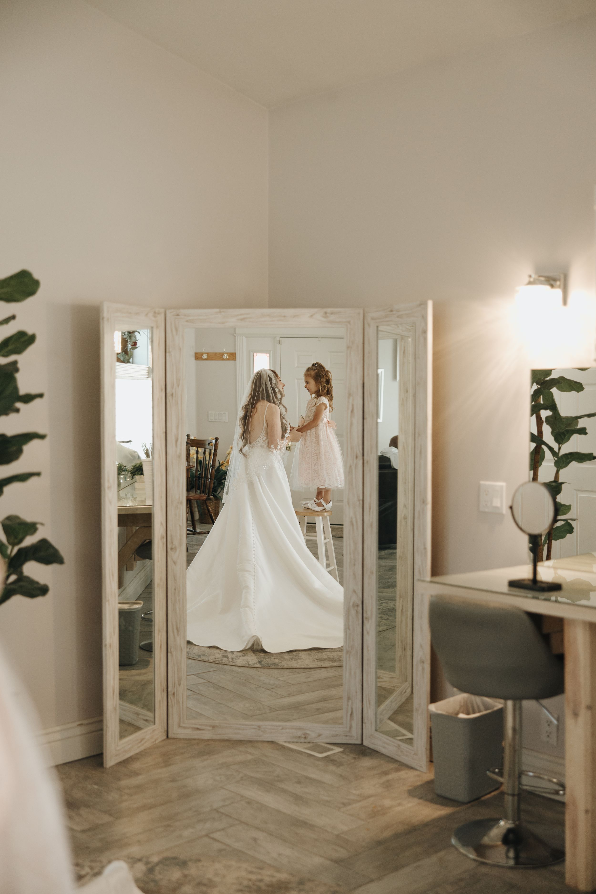 Bride admires wedding dress reflection in three-panel mirror during getting ready moments.