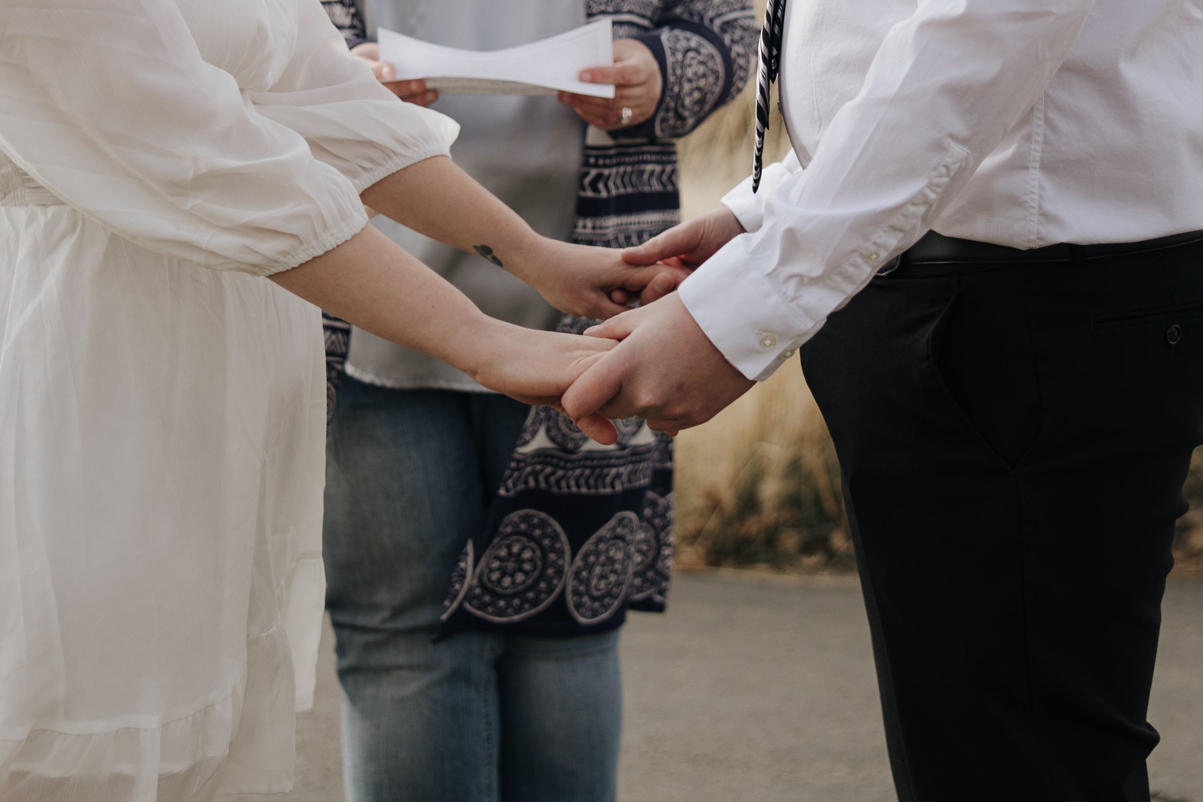 Close-up shot of three people holding hands together in a circle wearing white and denim outfits at sunset.