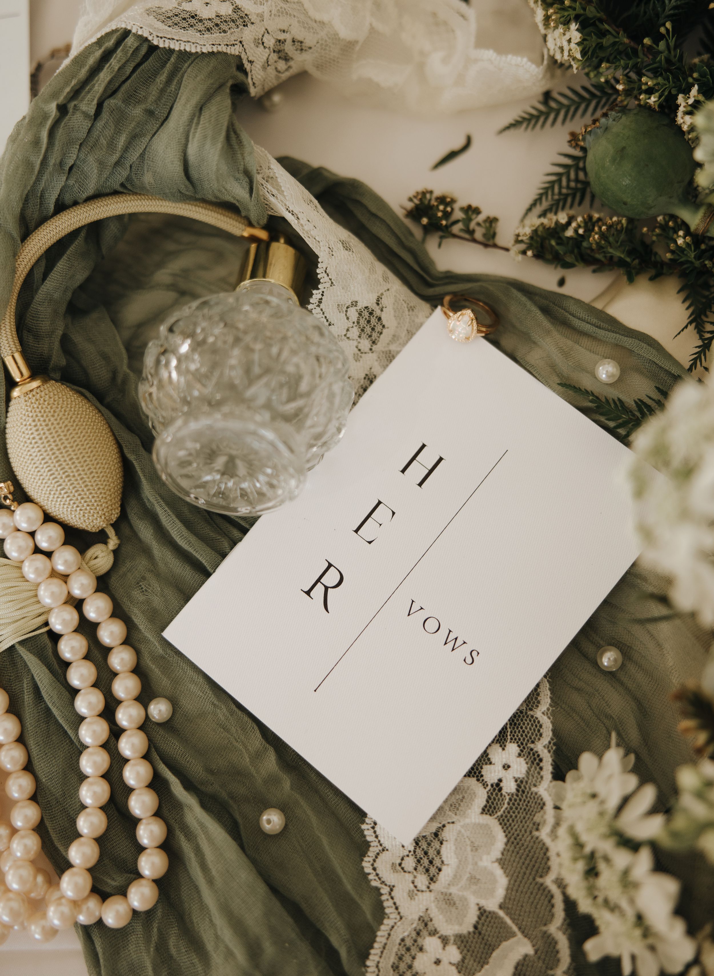 Wedding vow book with pearls and vintage accessories on textured fabric.