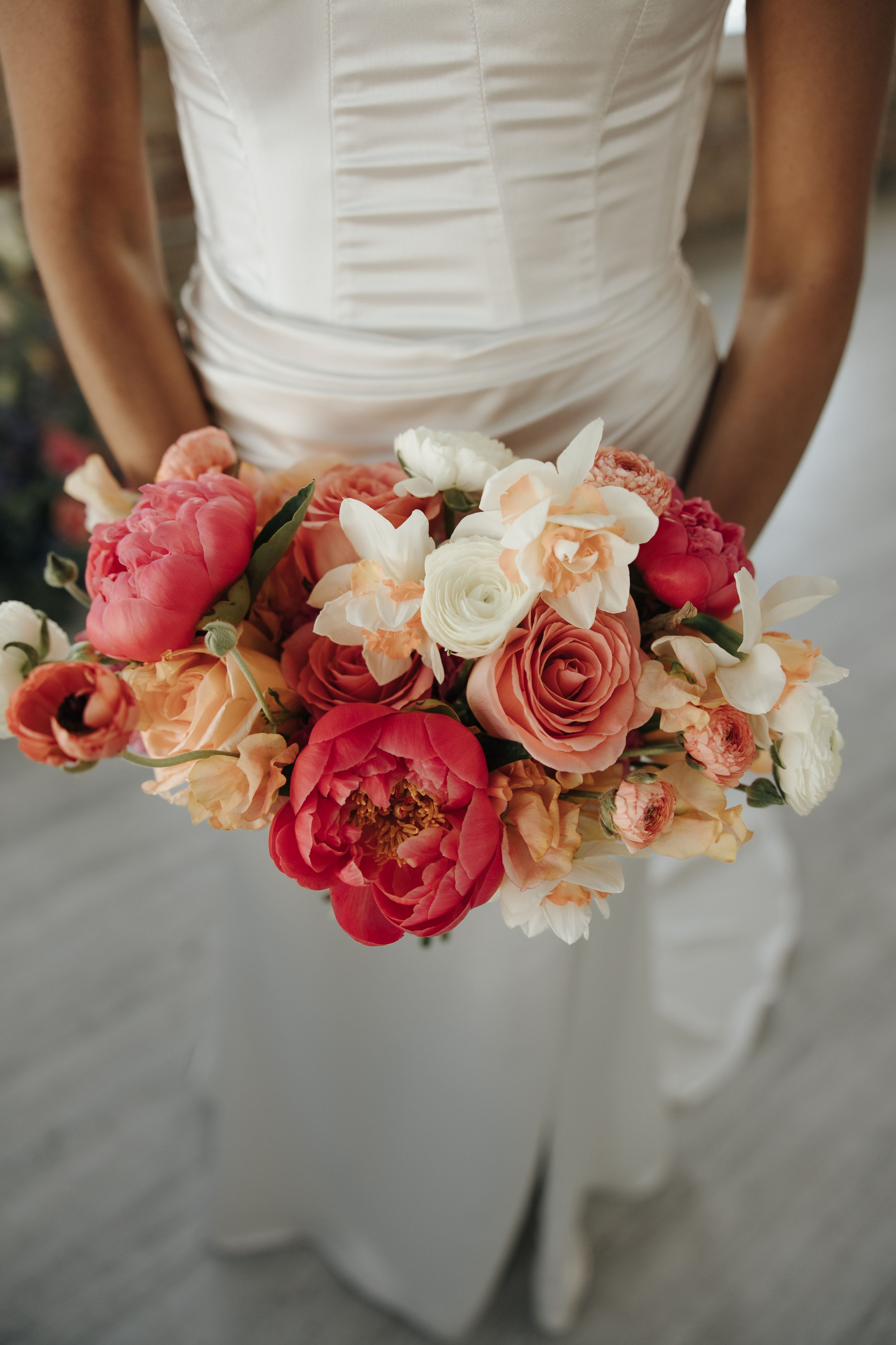 Bridal bouquet with pink peonies, peach roses, and cream flowers against a white dress.