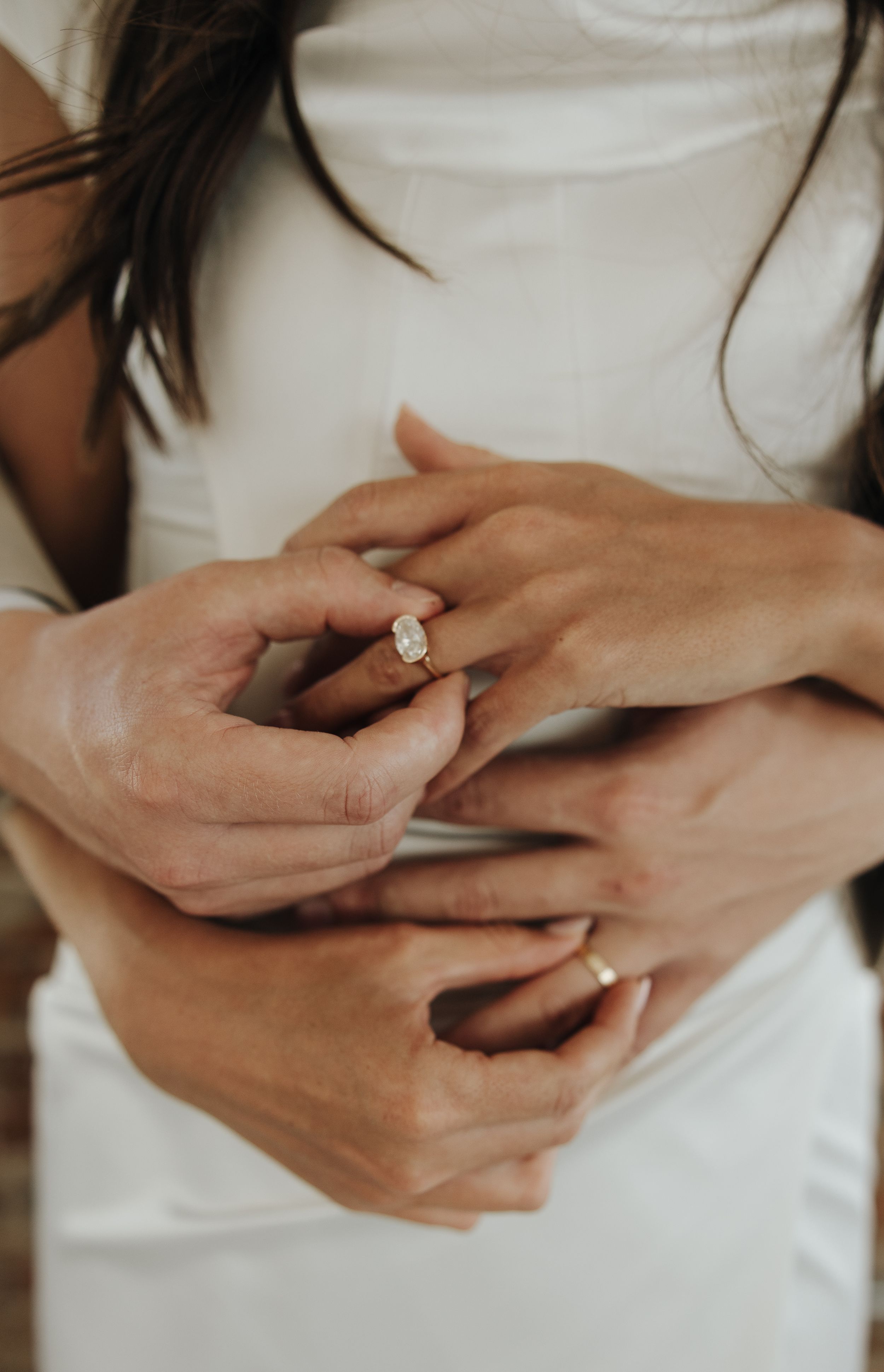 Close-up of hands wearing an engagement ring against a white dress.
