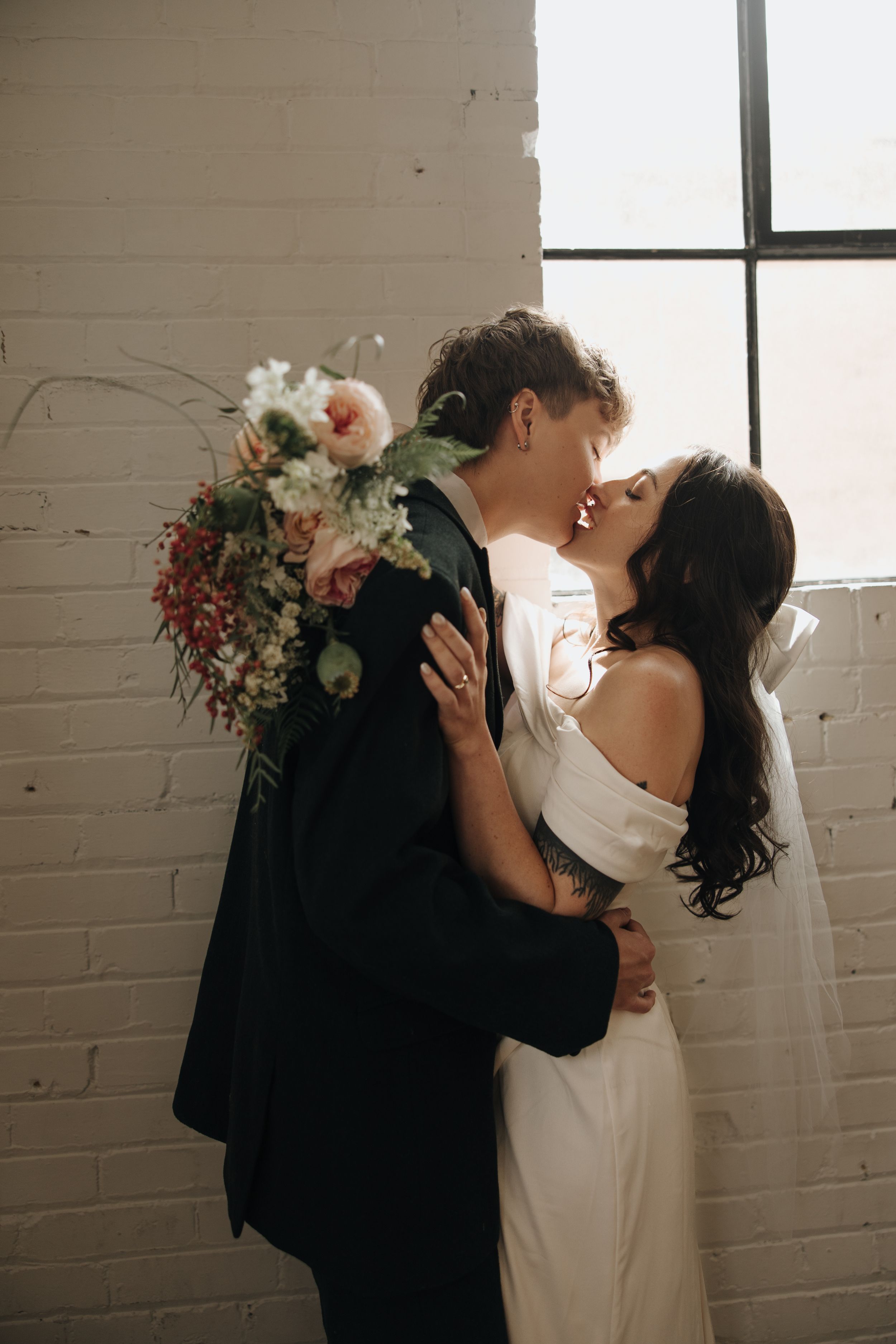 Romantic wedding moment against white brick wall with delicate floral bouquet.