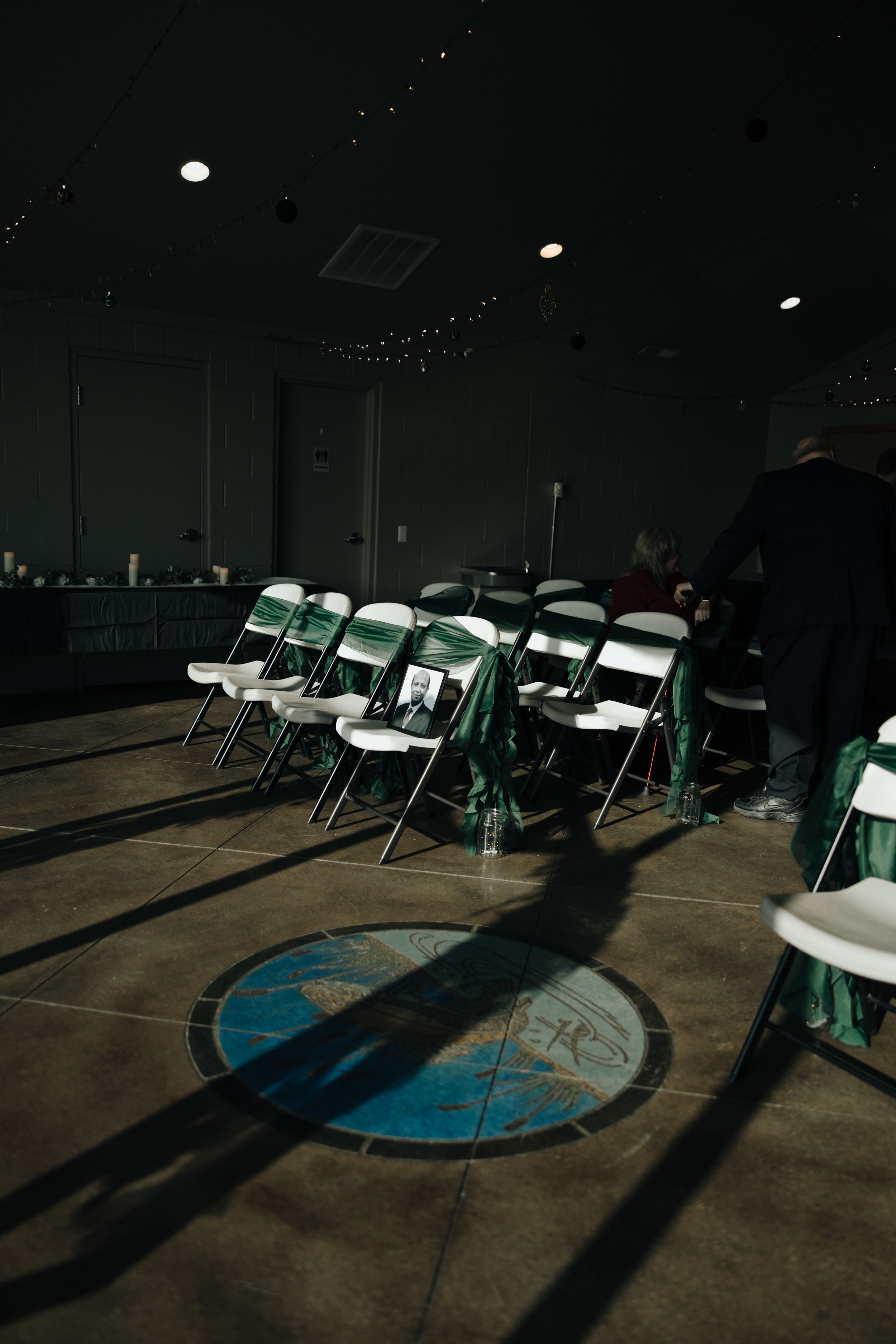 Green metal folding chairs arranged in rows cast shadows on a concrete floor with a circular blue design element.