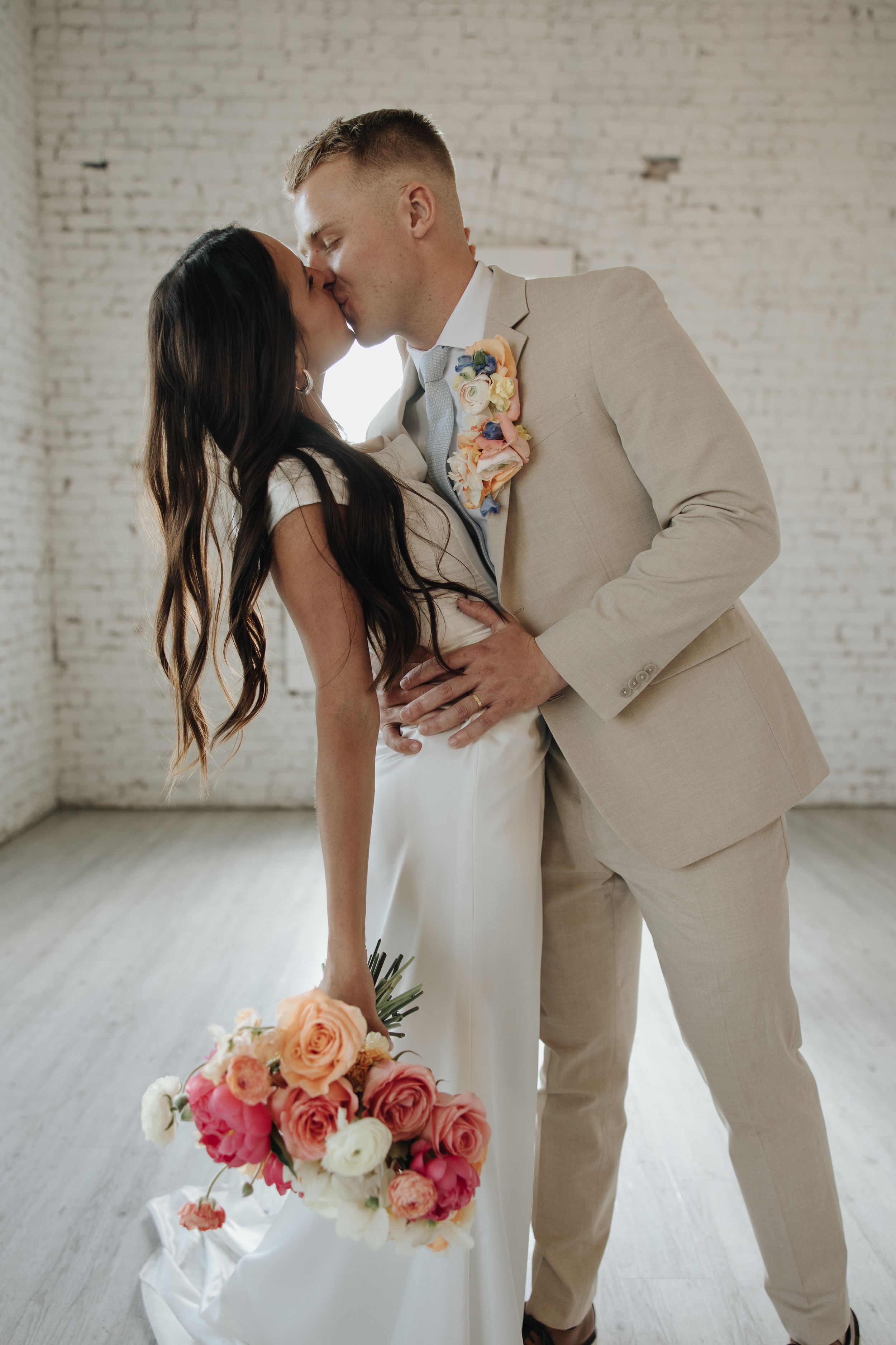 Romantic wedding portrait with colorful bouquet against white brick wall and wooden floors.