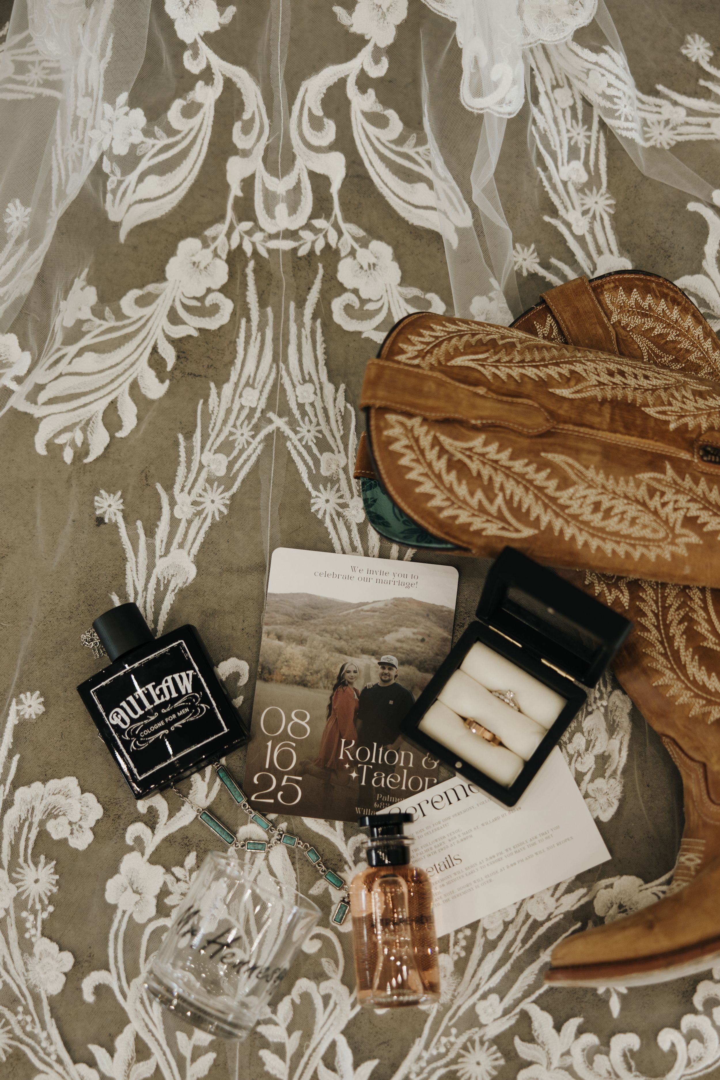 Vintage leather cowboy boots arranged with perfume bottles and cosmetics on a floral patterned background.