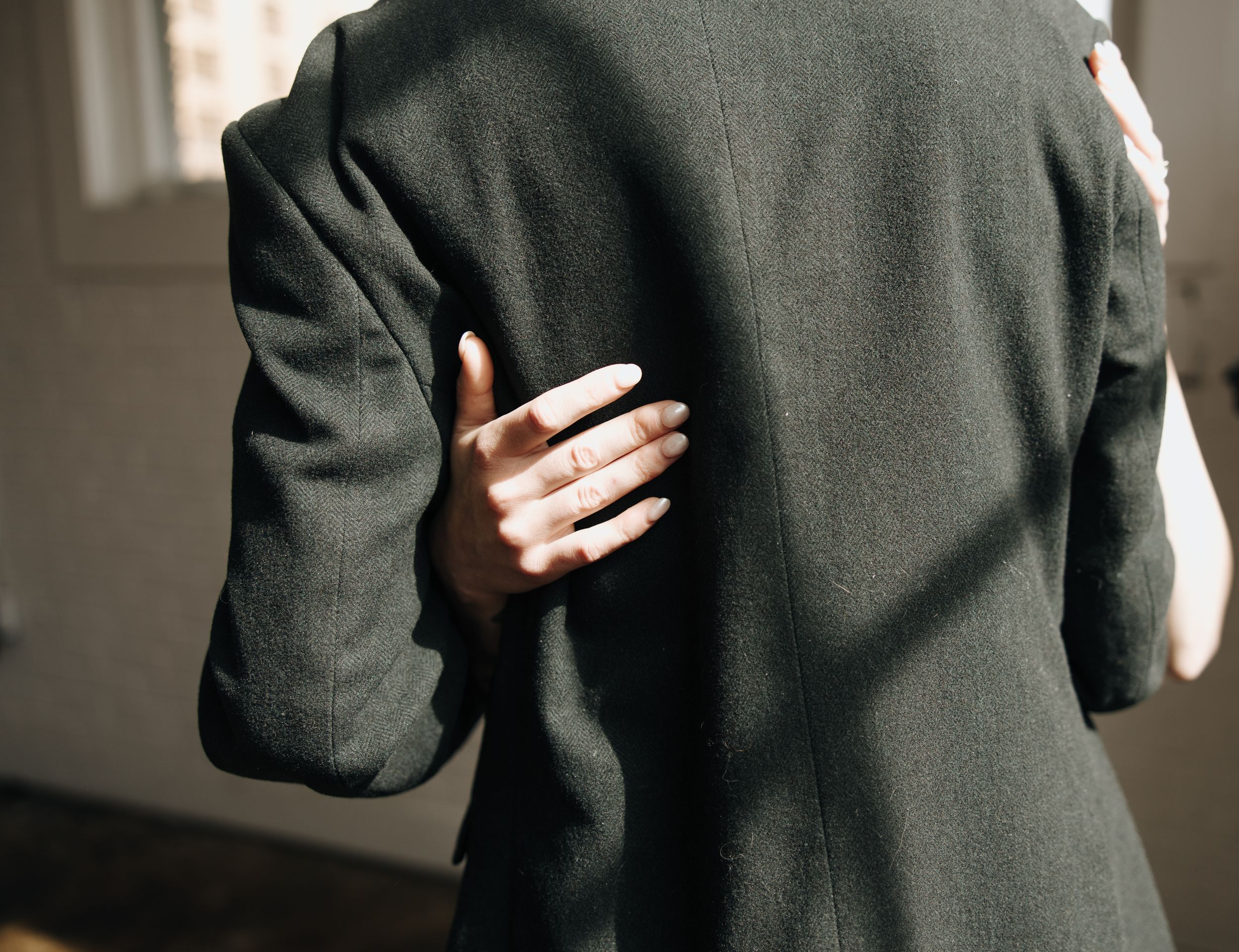 Close-up of hand resting on dark suit jacket during intimate moment.