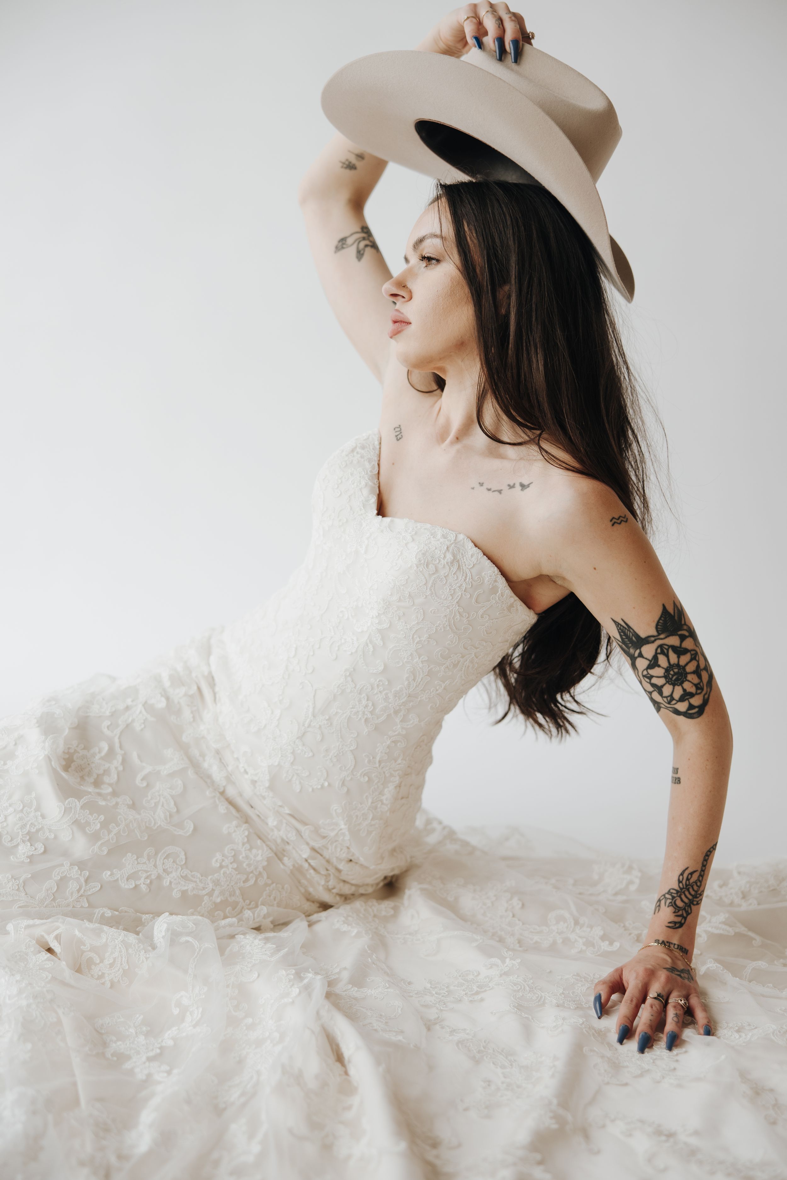 Artistic bridal portrait with woman in white dress wearing cowboy hat showing tattoos.