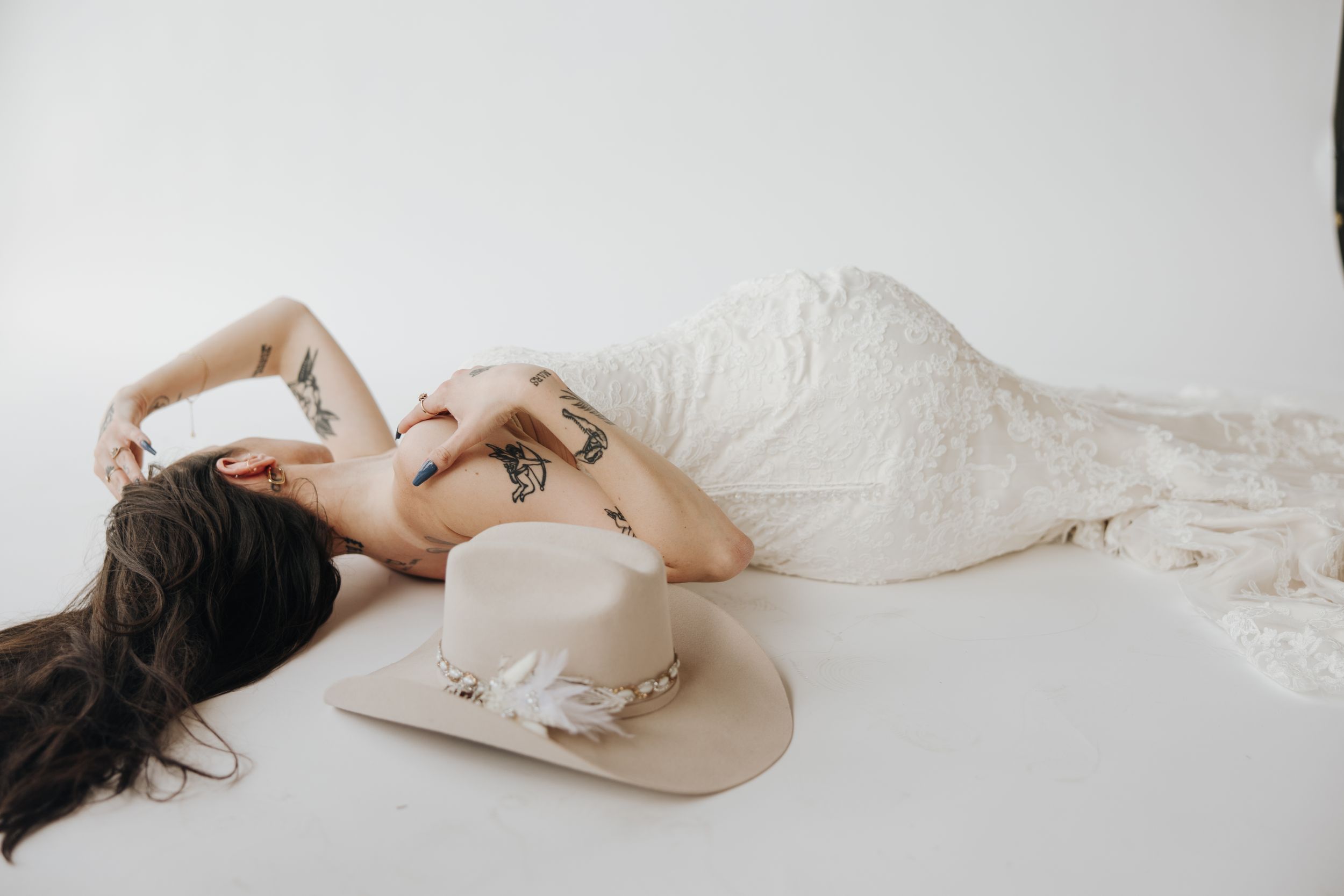 Woman in lace wedding dress lying down with cowboy hat in artistic pose.
