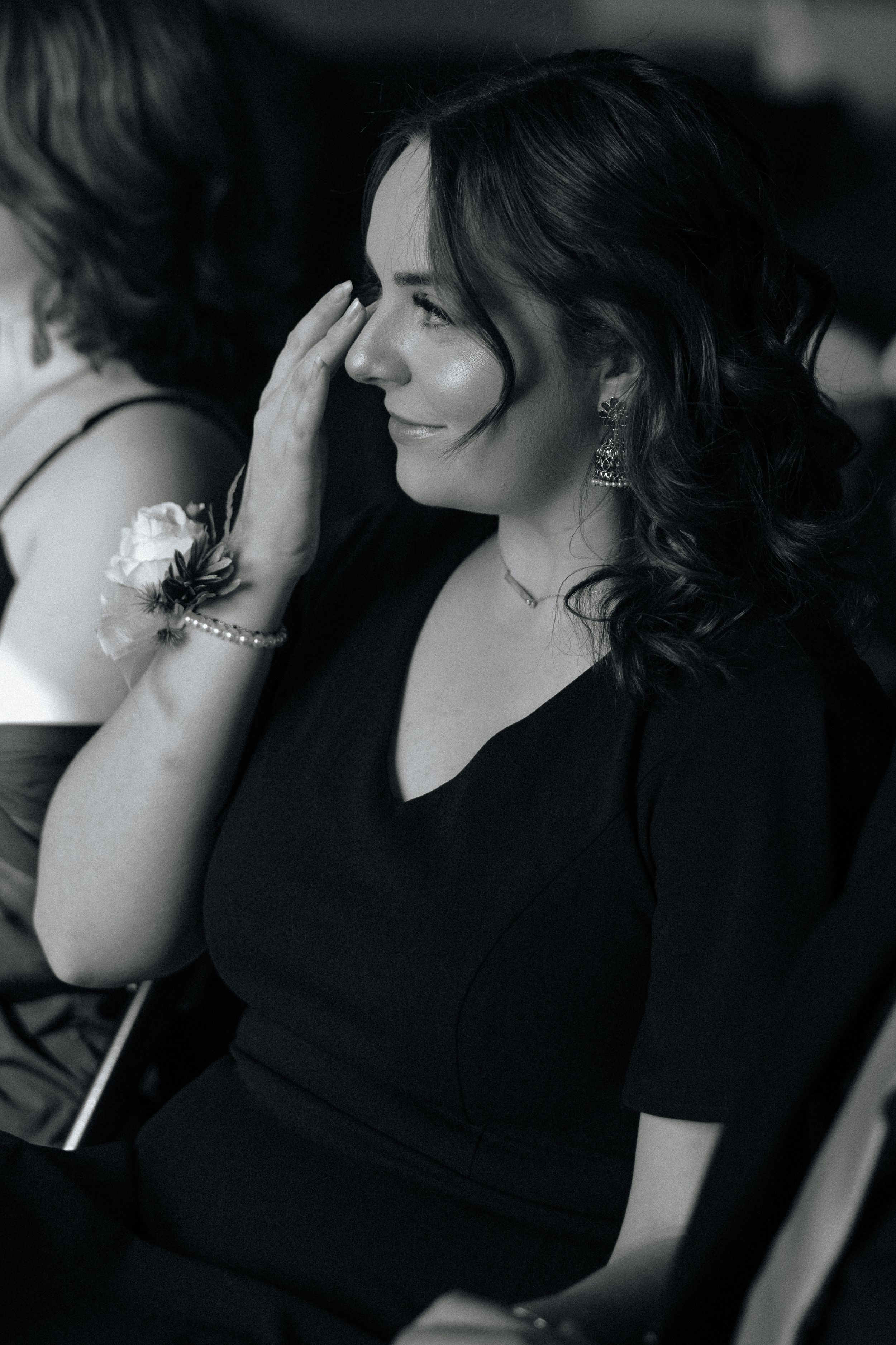 A woman in a black top smiles warmly while seated indoors in black and white photography.
