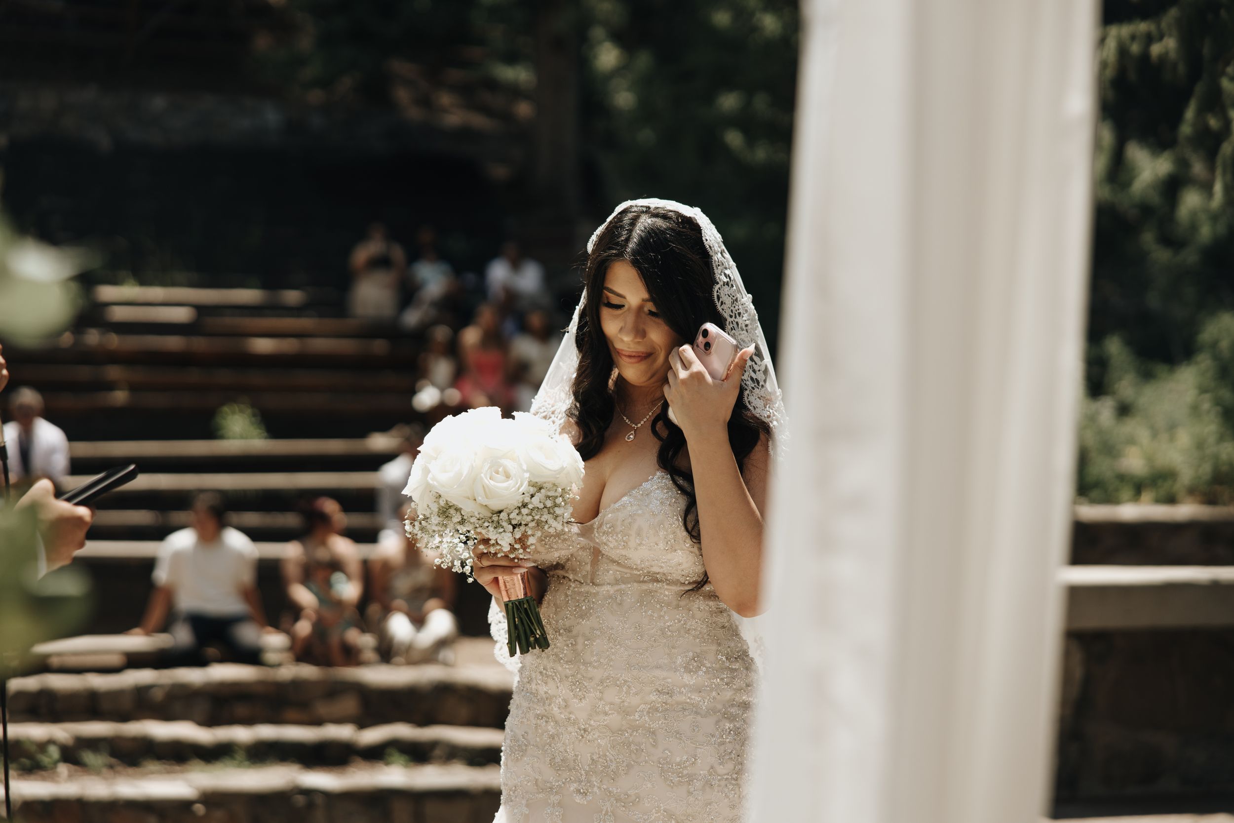 Bride in lace gown holds white bouquet while walking down outdoor stone steps.