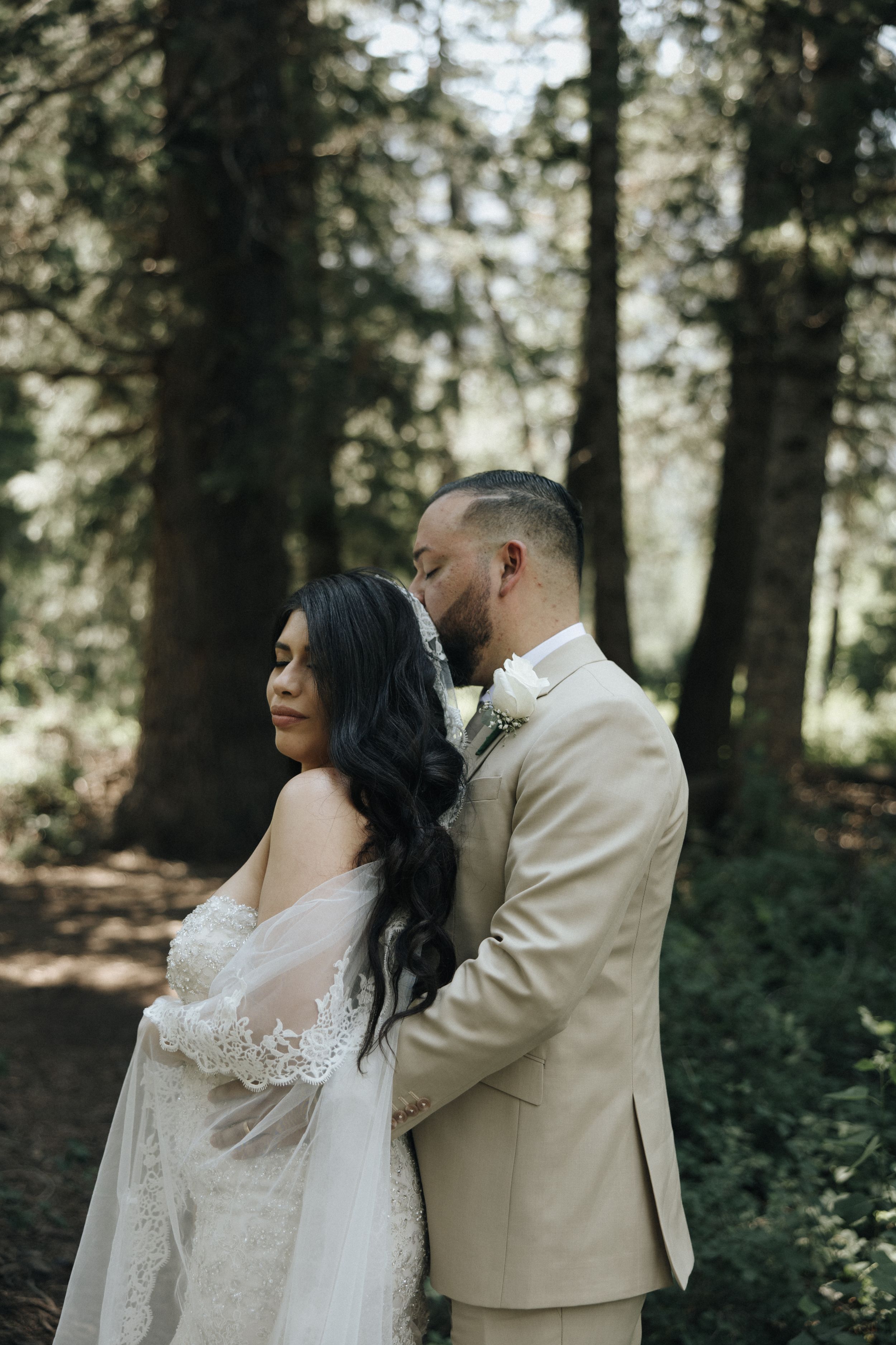 Romantic couple poses in sunlit forest wearing wedding attire.