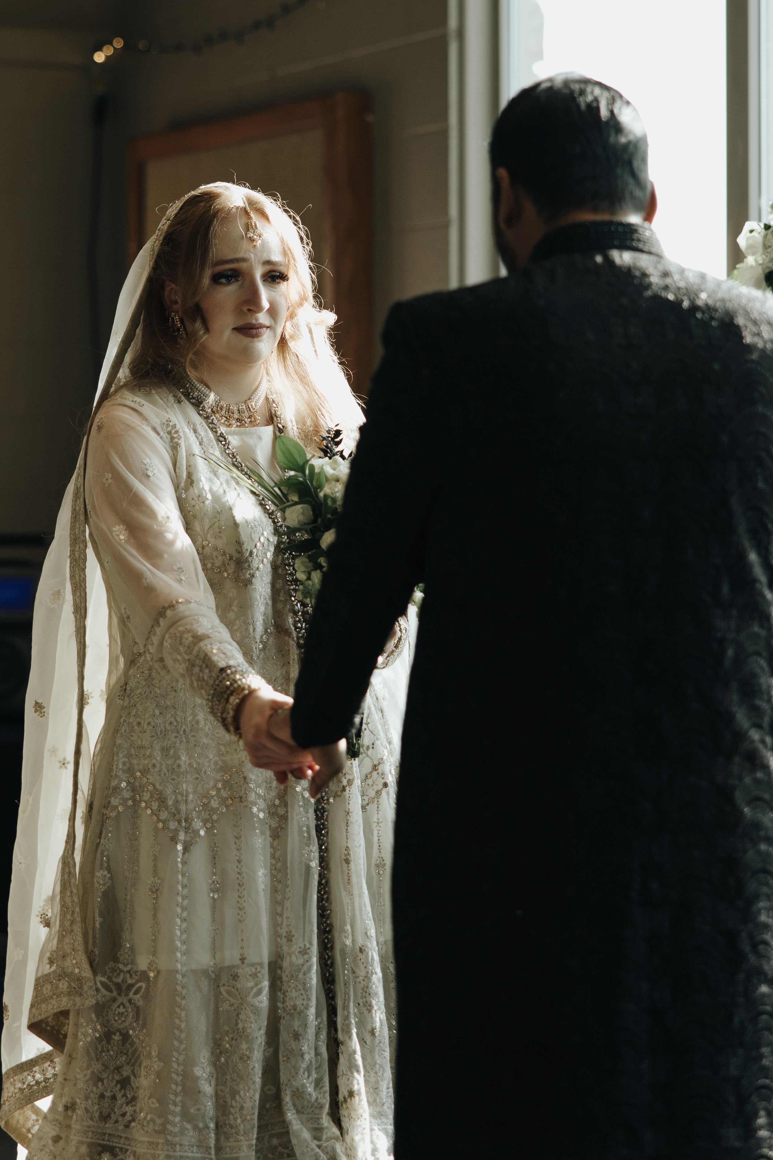 Couple shares an intimate moment during their wedding ceremony as bride wears an ornate white lace gown with veil.