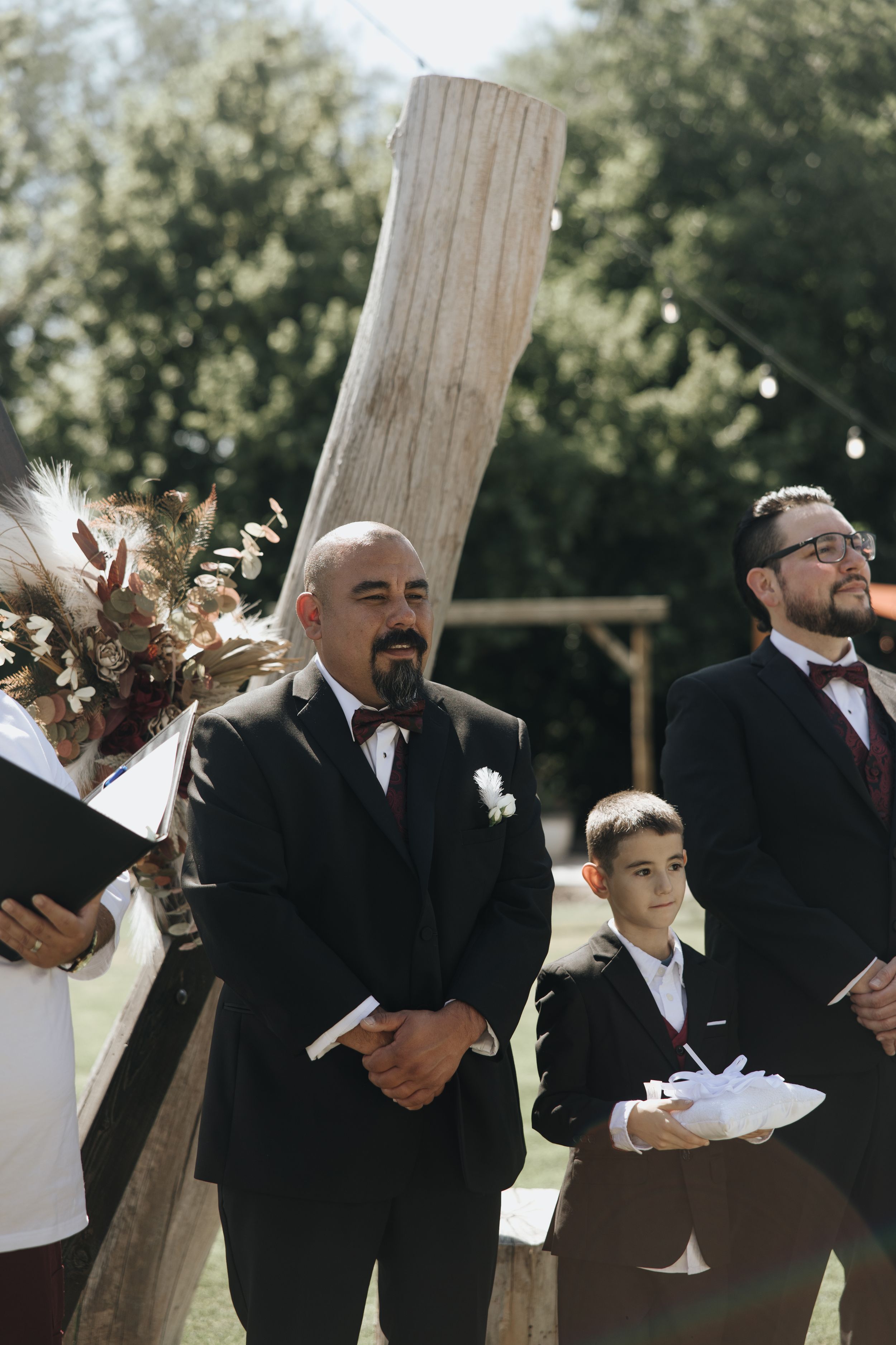 Wedding ceremony participants standing at a rustic wooden altar outdoors.