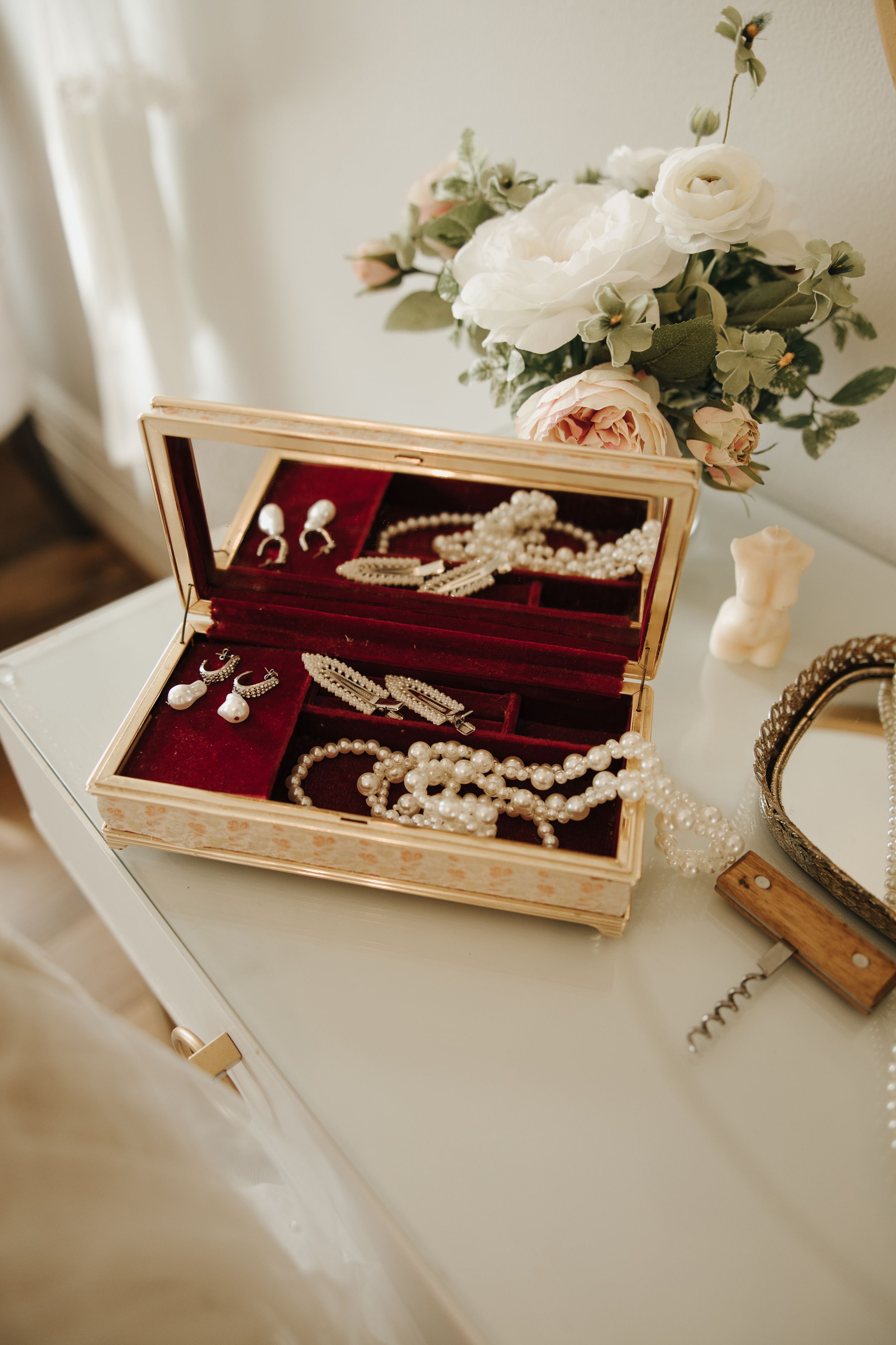 Vintage jewelry box displaying pearl necklaces and accessories with white roses in background.